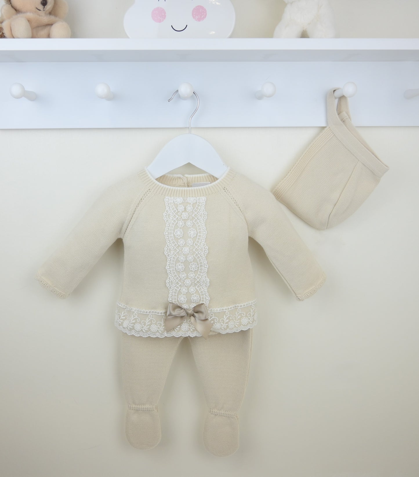 Beige baby outfit with lace details on a white surface