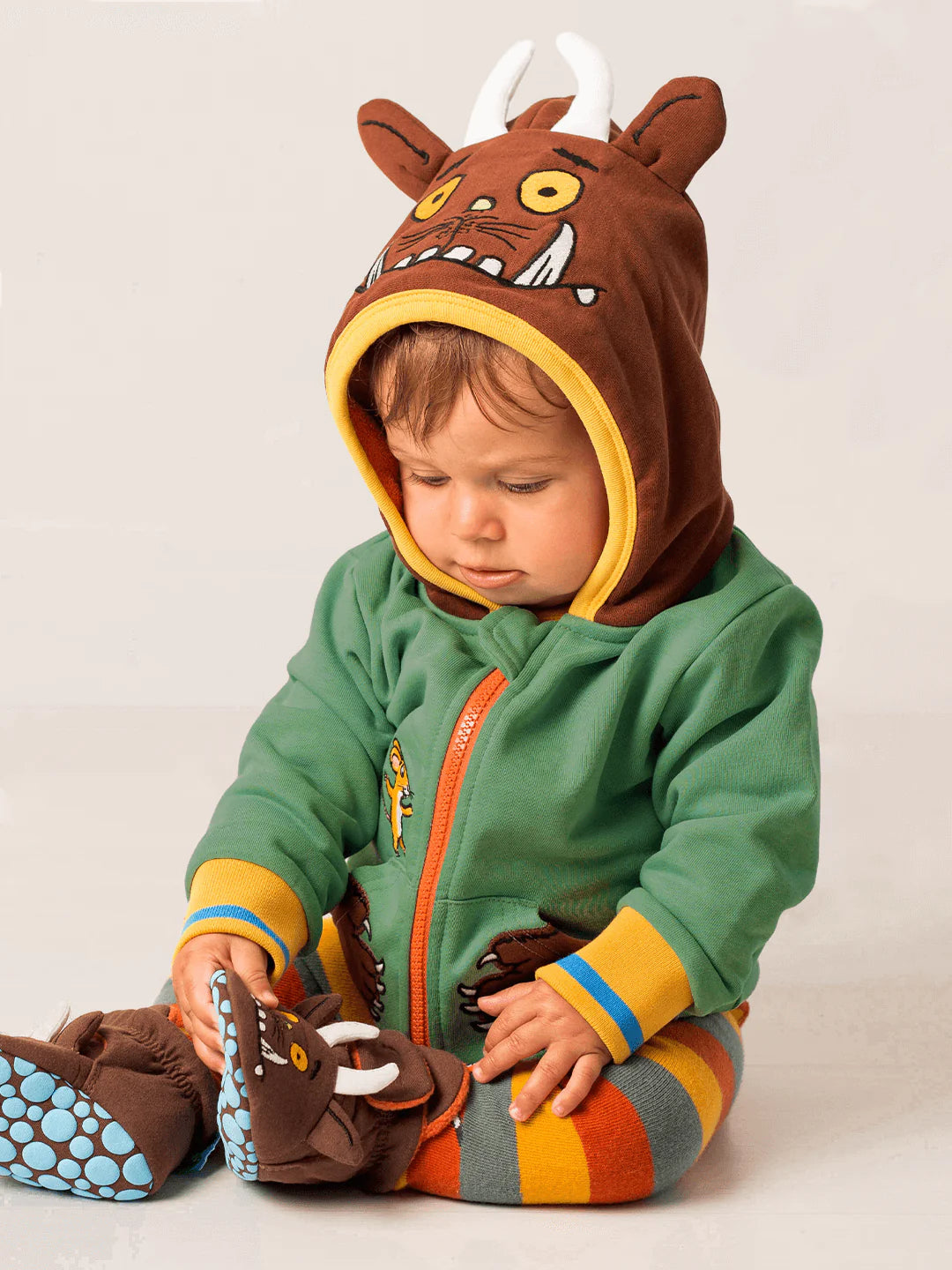 Child wearing a green and brown outfit with gruffalo face on a plain background