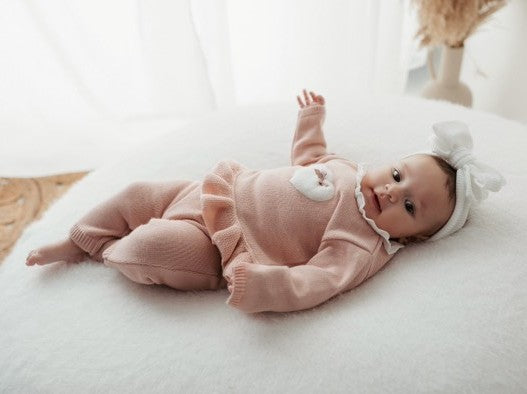 Baby in a pink outfit with a white bow lying on a white surface