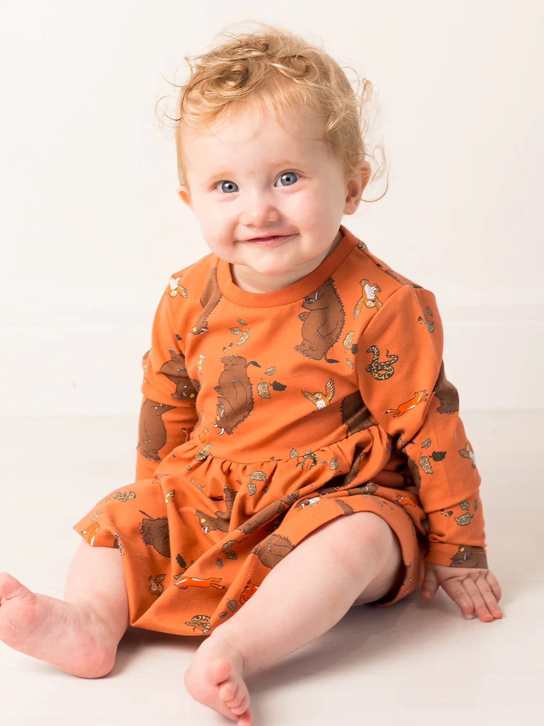 Child wearing an orange dress with gruffalo patterns on a white background