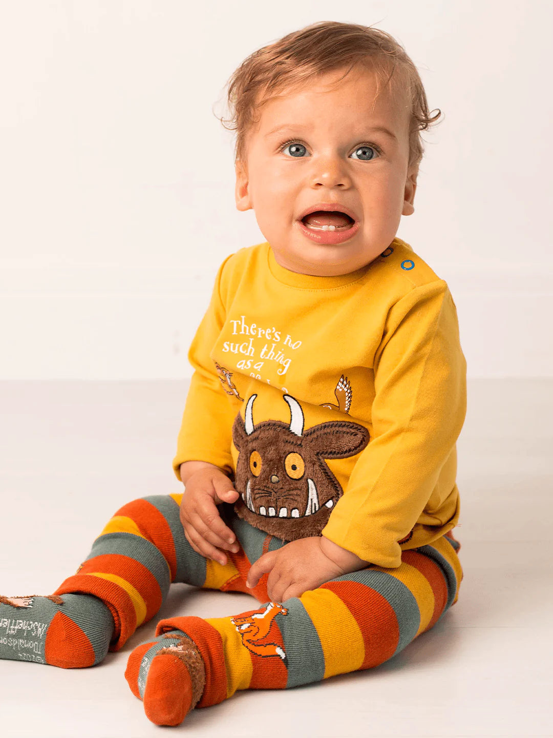 Baby wearing a yellow outfit with a gruffalo character on a white background
