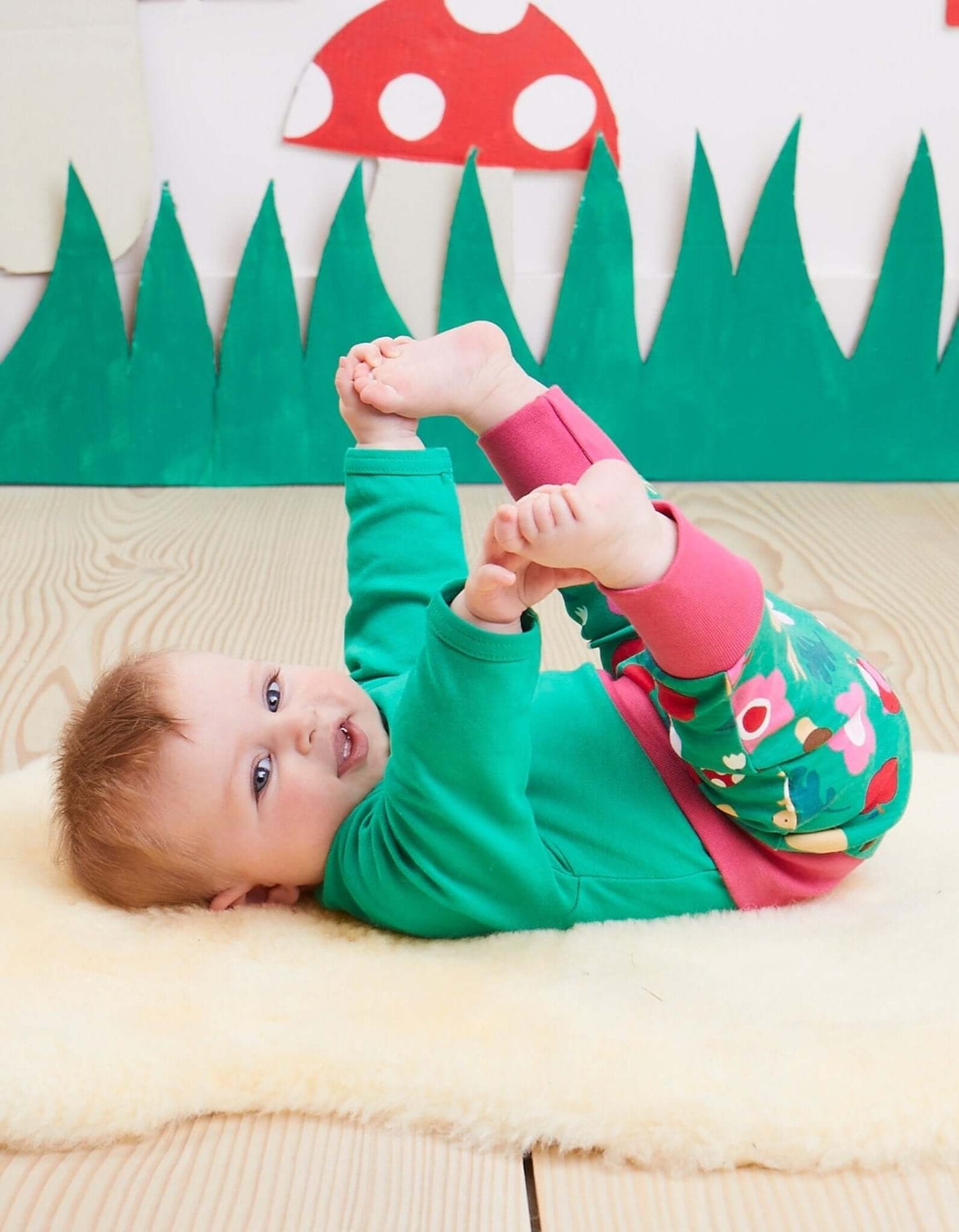 Baby lying on a wooden floor with colorful mushroom decorations in the background