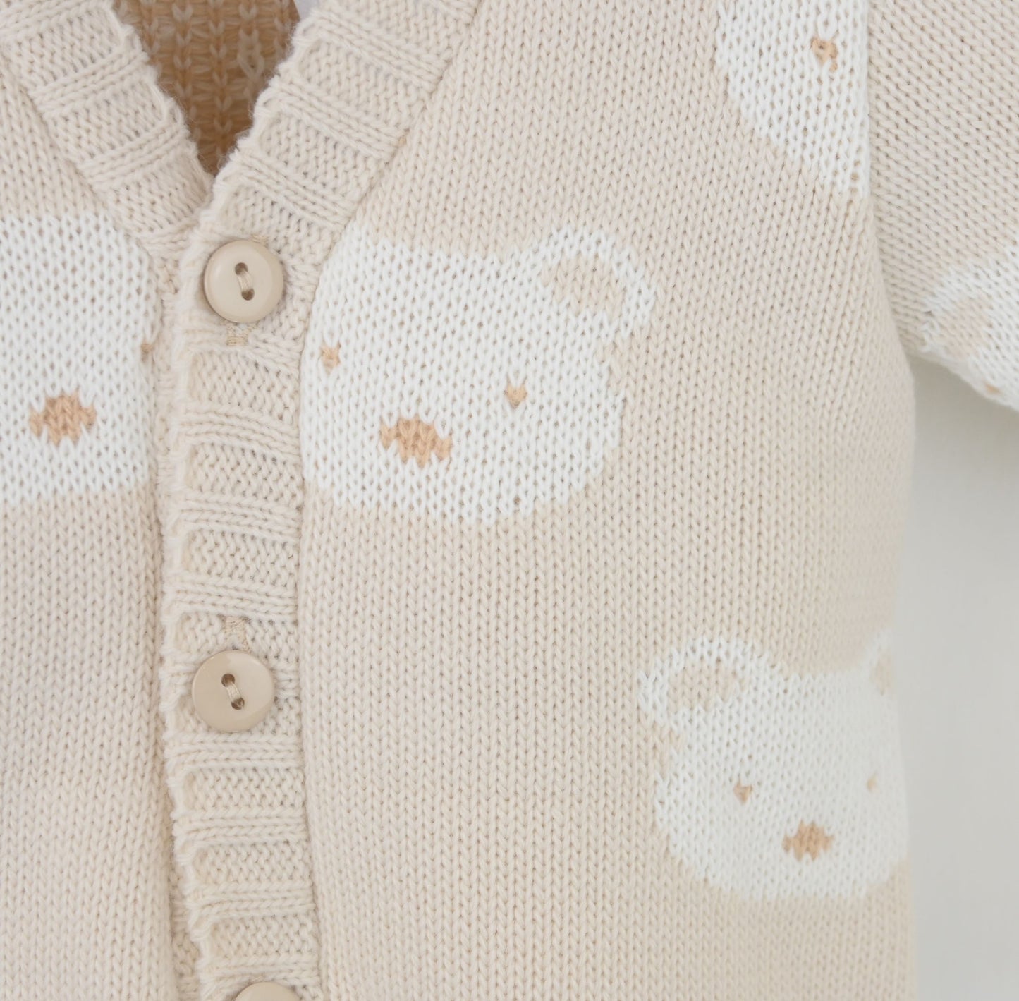 Close-up of a beige knitted cardigan with button details and subtle pattern.