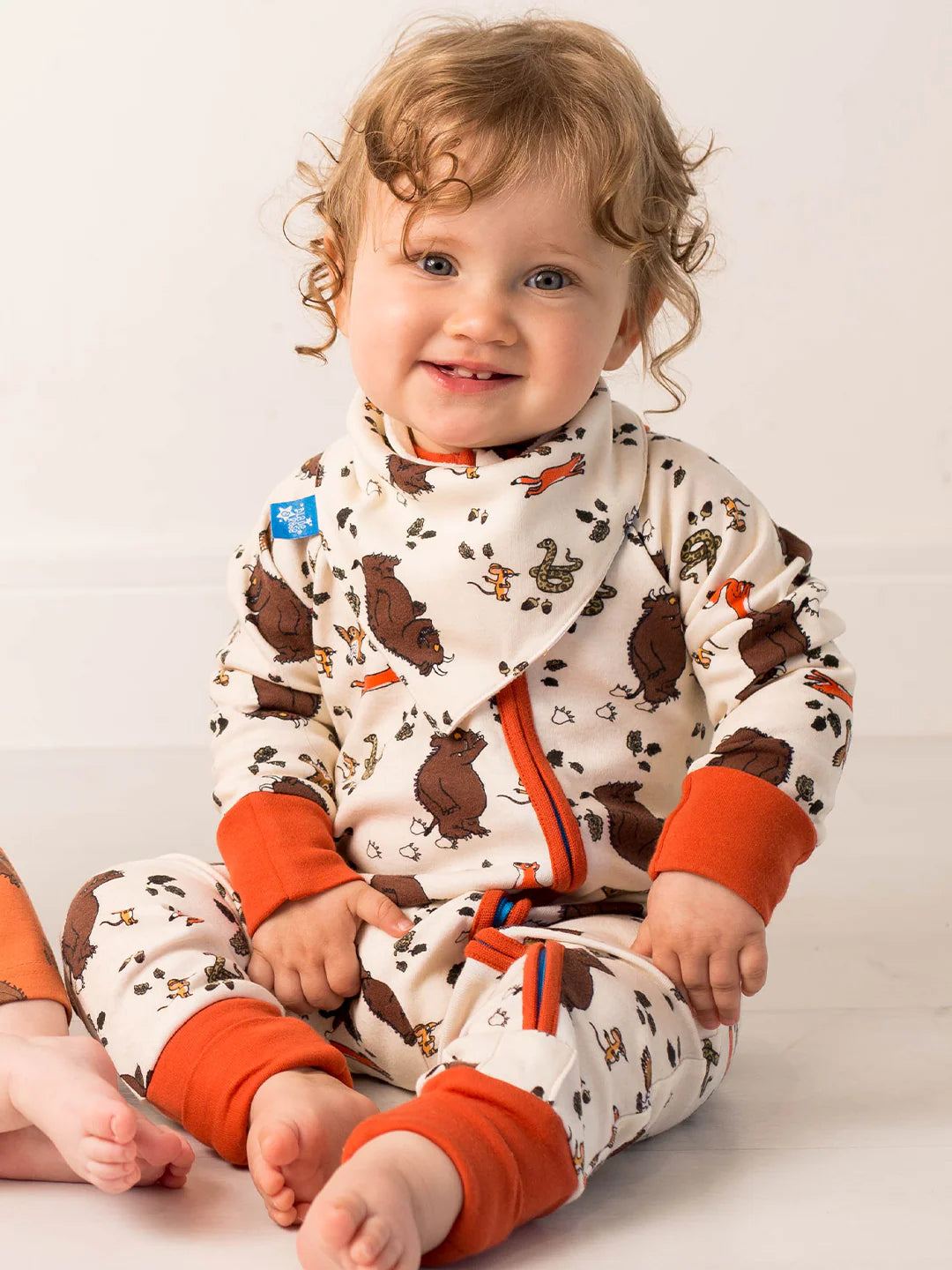 Child wearing a patterned outfit with brown and orange elements on a plain background