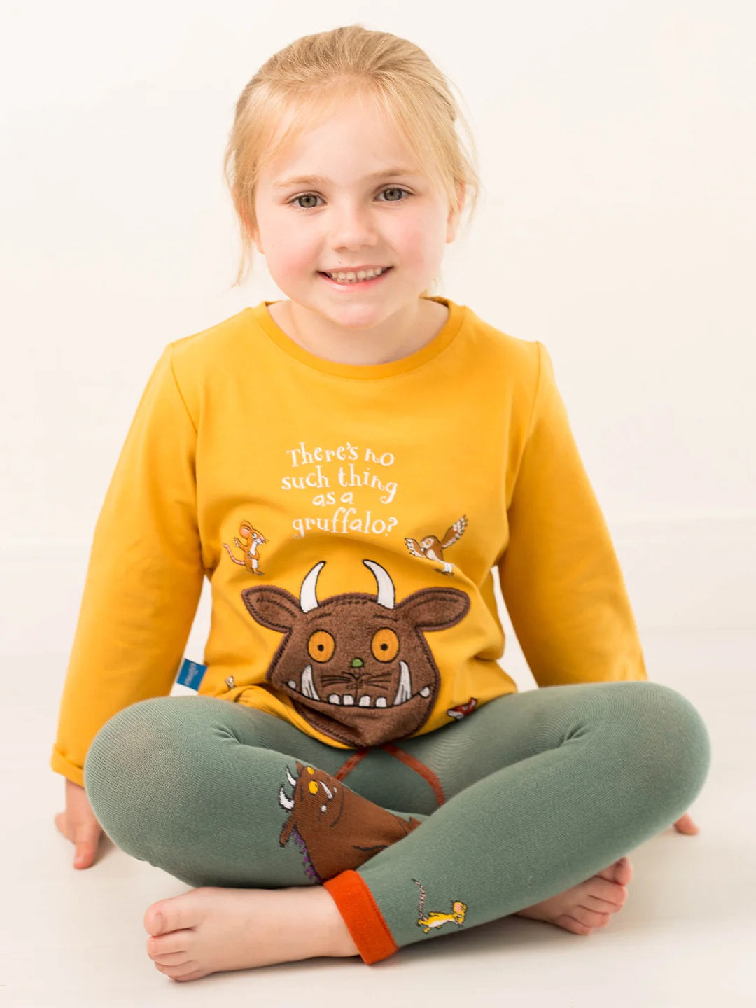 Child wearing a yellow tshirt with a Gruffalo cartoon character and green pants on a white background