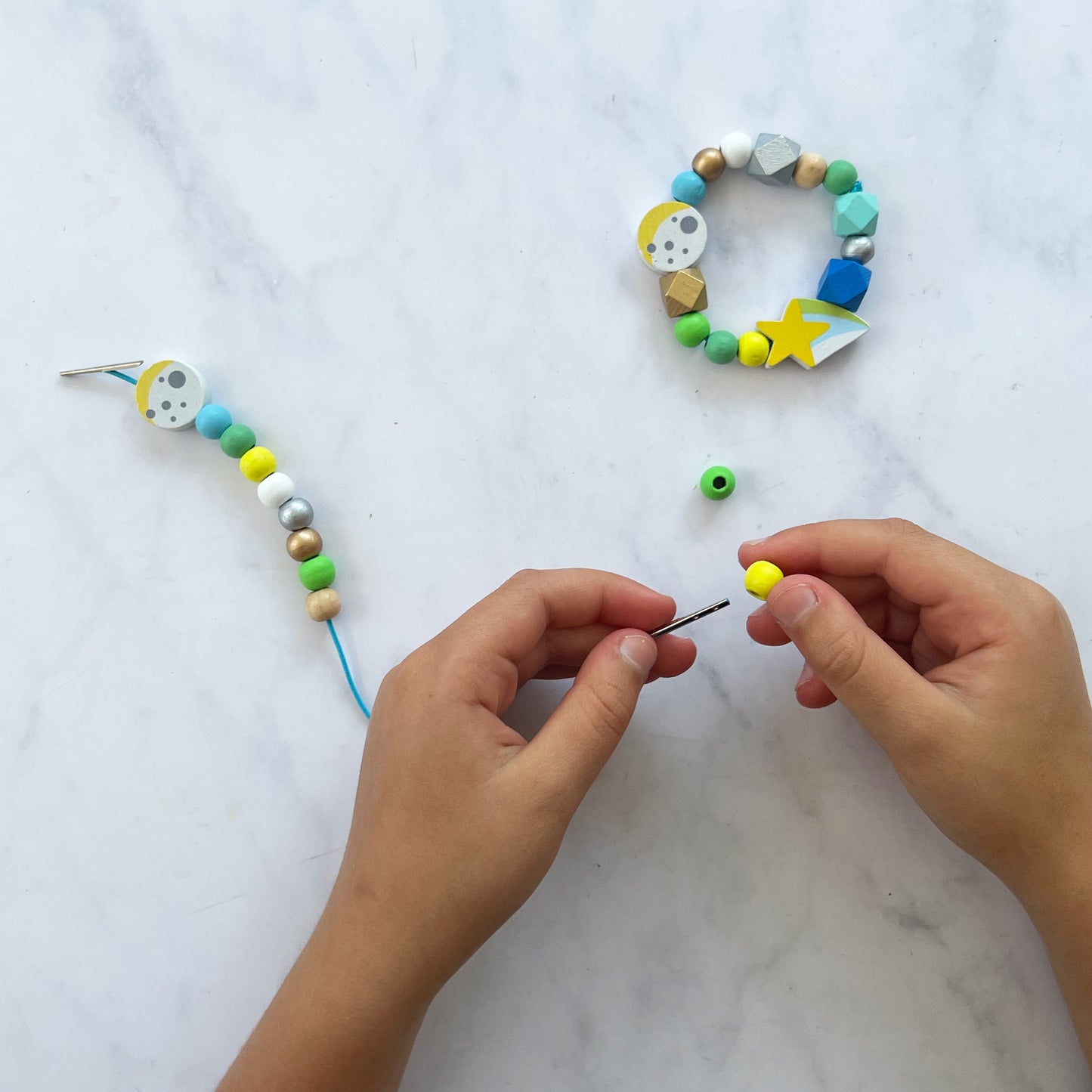 Hands working on a beaded necklace with colorful beads on a marble surface