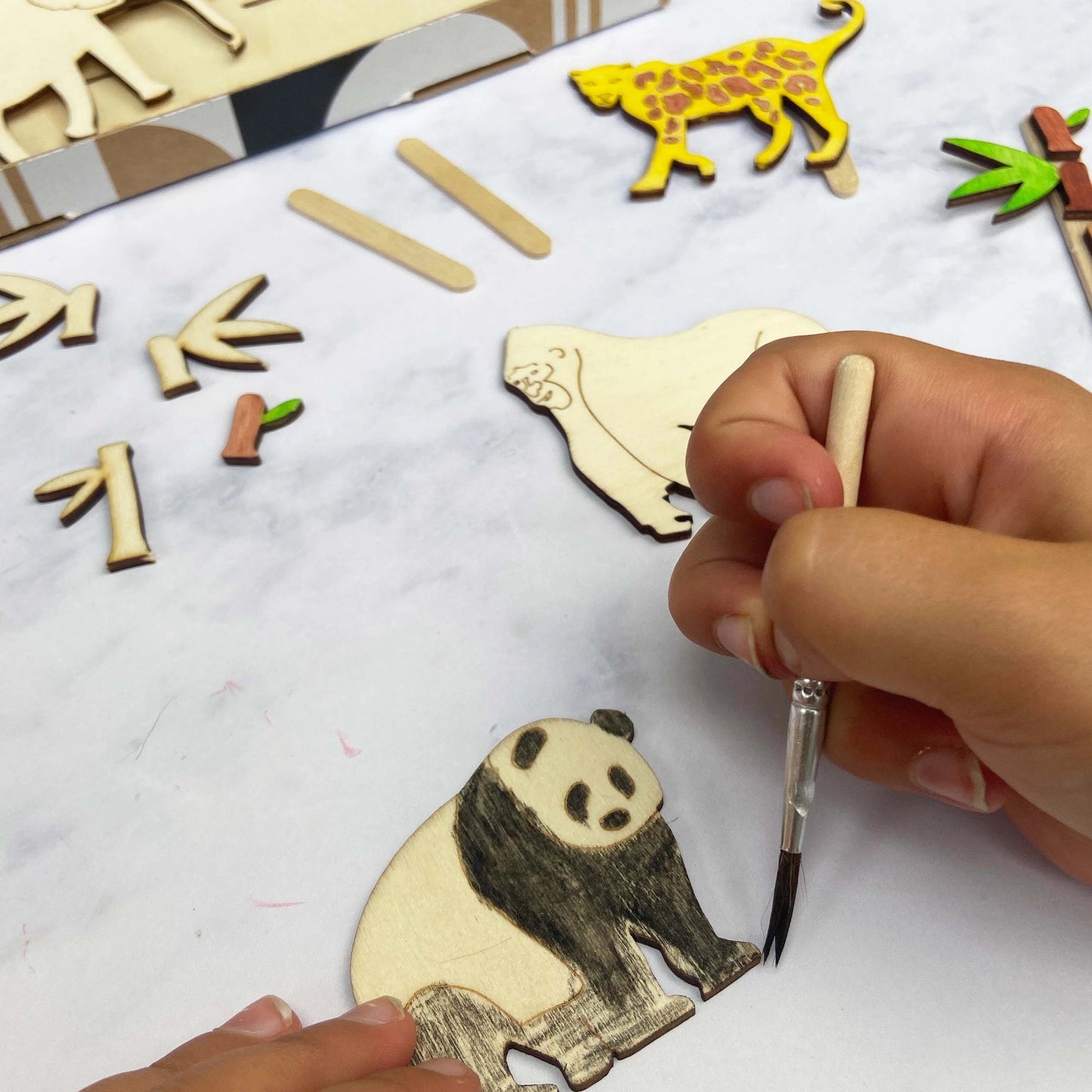 Hand painting a wooden panda figure with a brush on a white surface.