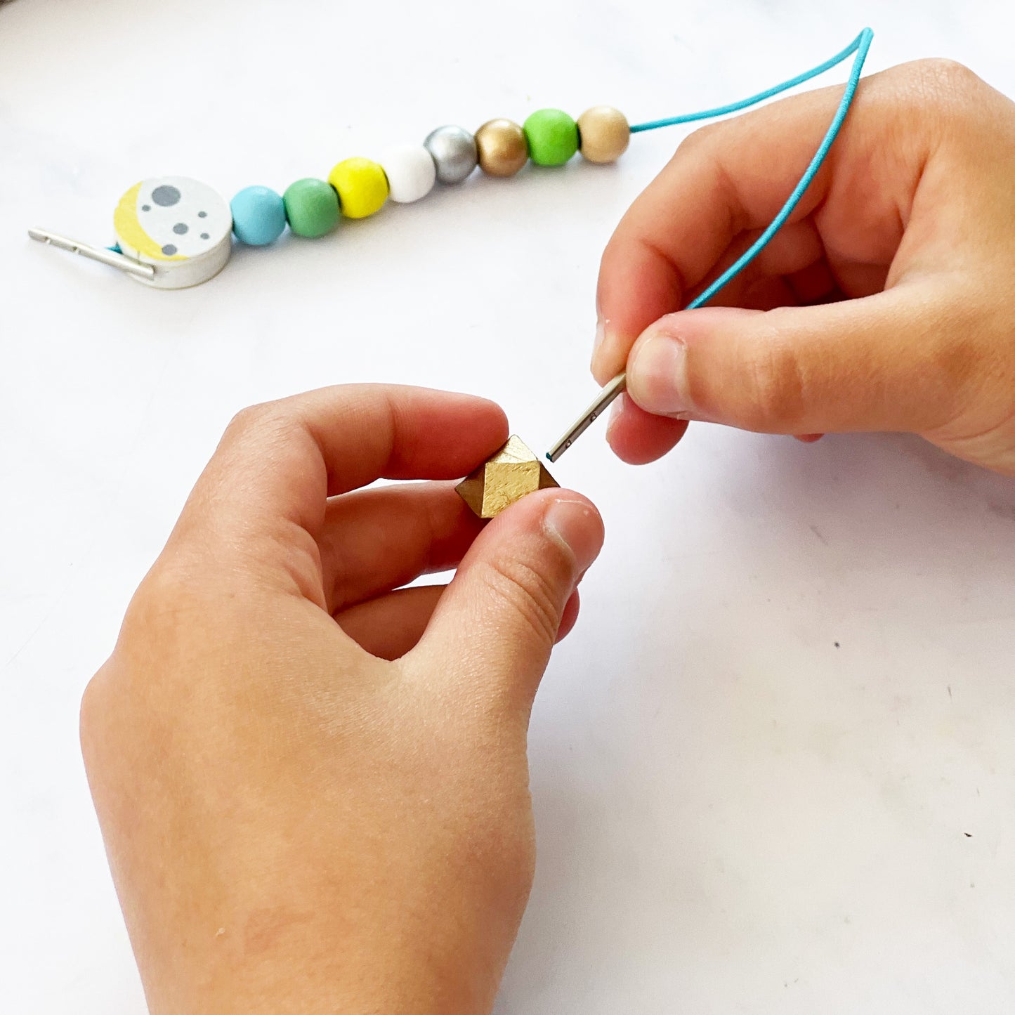 Hands threading beads on a string with a white background