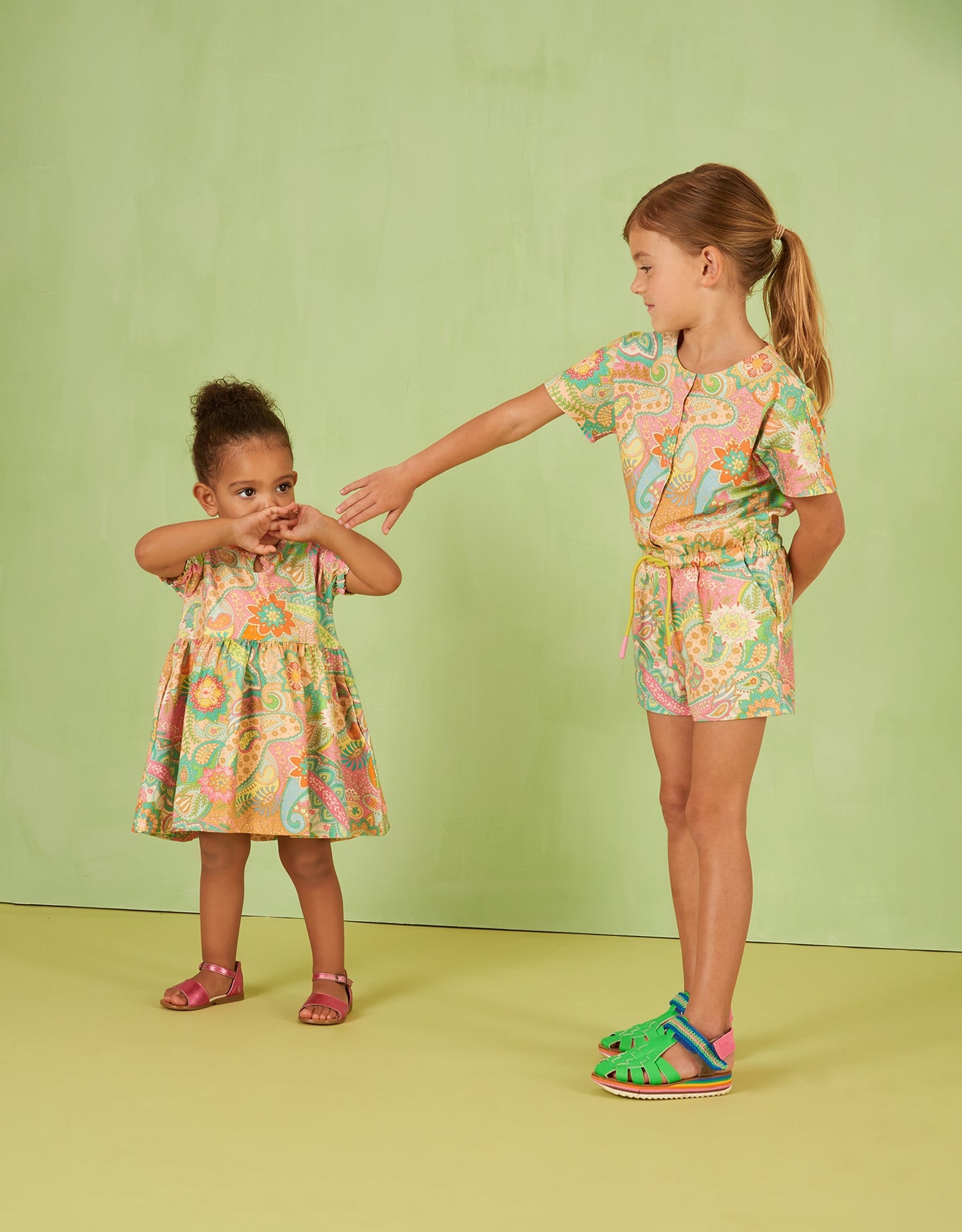 Two children wearing matching floral Oilily paisley outfits on a green background