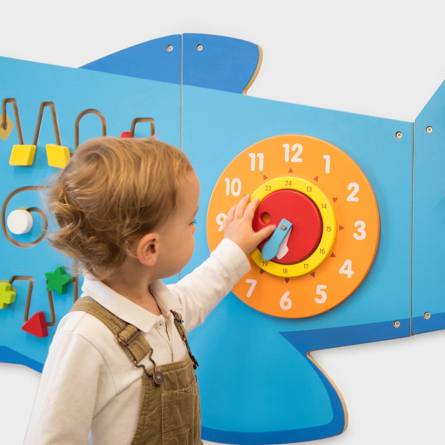 Child interacting with a colorful educational wall panel featuring numbers and shapes.