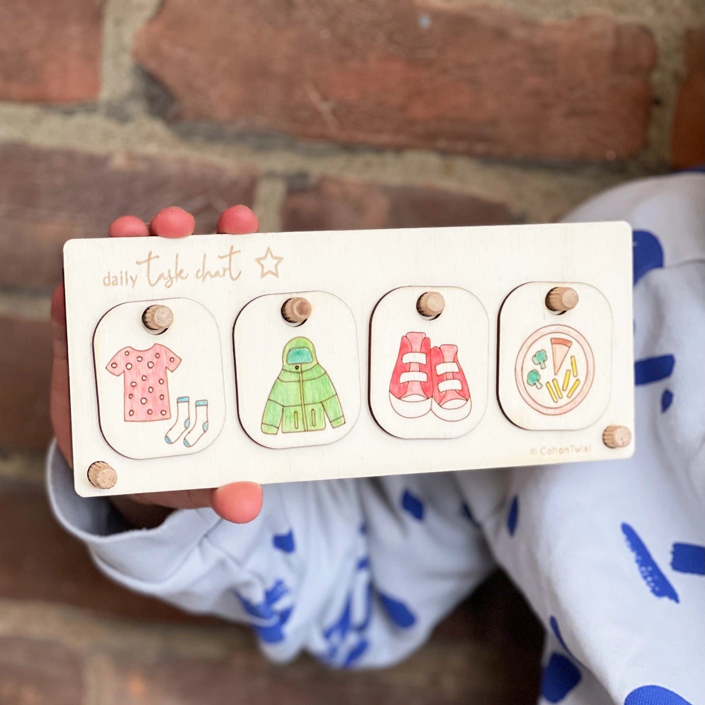 Wooden toy with colorful illustrations held by a child against a brick wall.