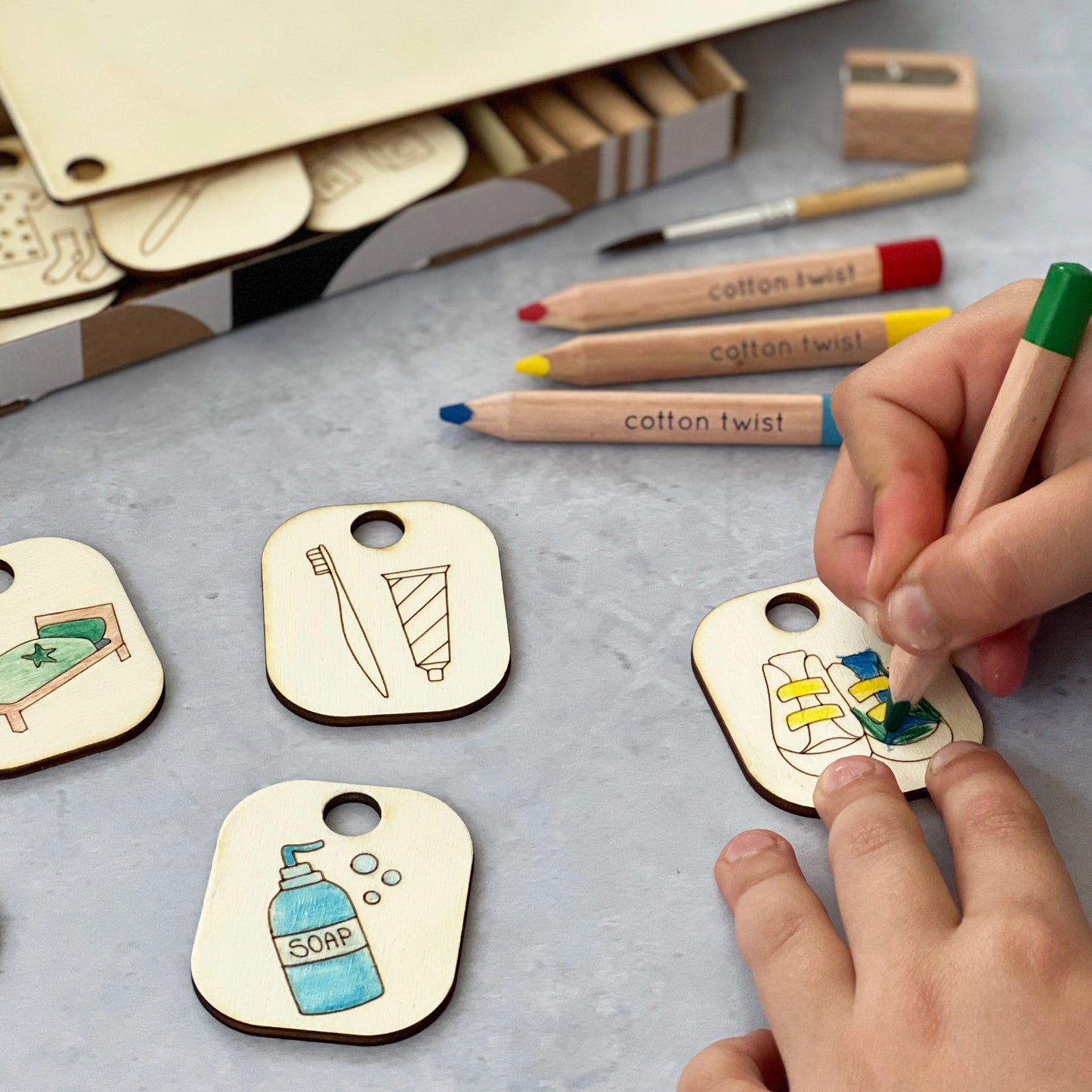 Child coloring wooden tags with markers on a gray surface