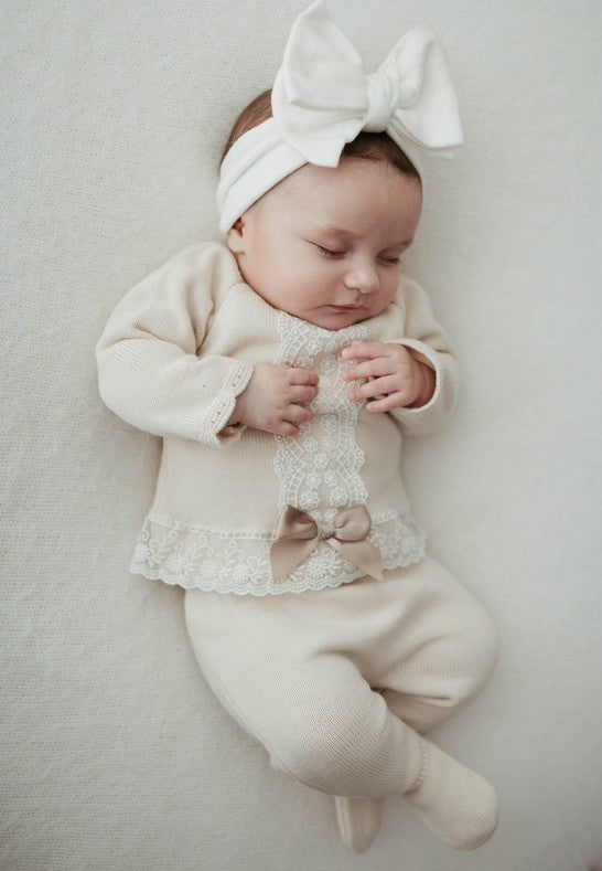 Baby in a natural lace outfit with a bow headband on a light background