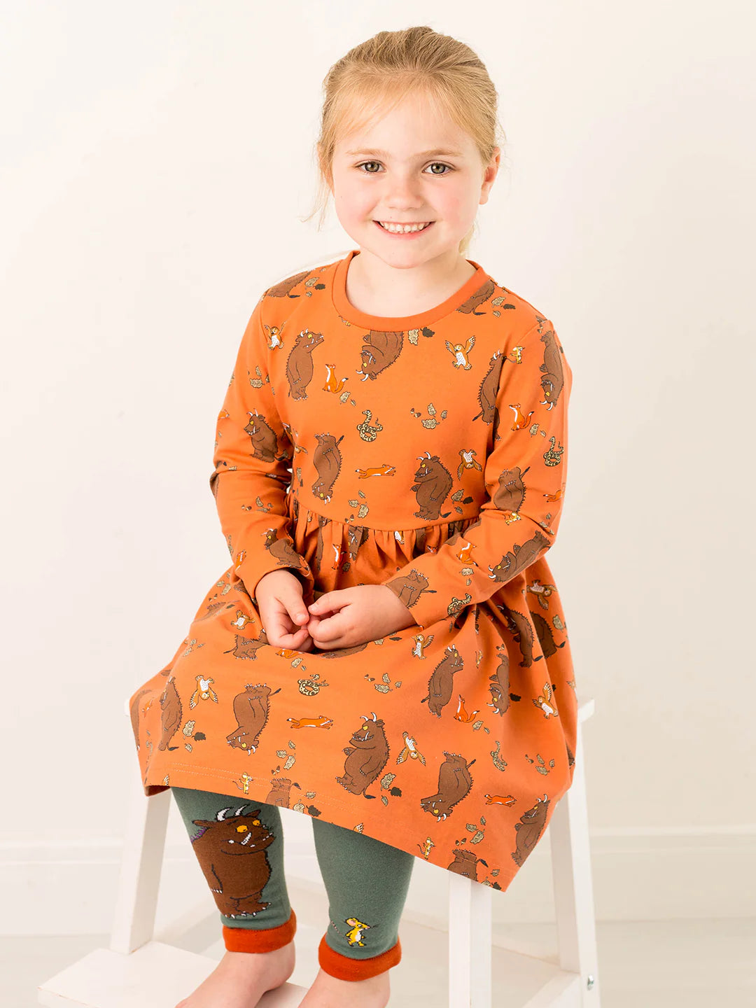 Young girl wearing an orange dress with gruffalo print on a white background