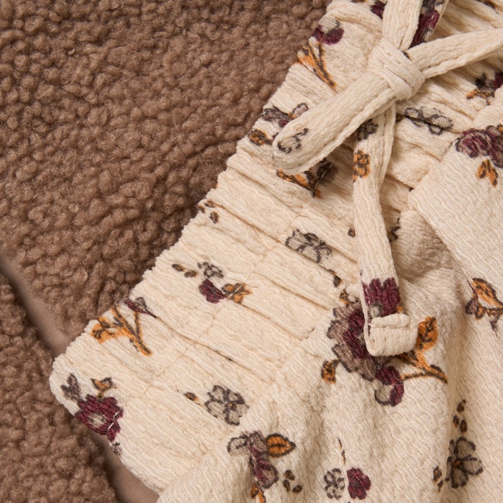 Close-up of a textured borg fabric gilet with floral patterned skirt on a brown surface