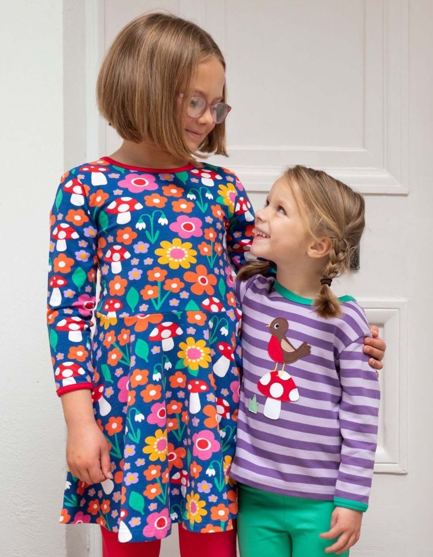 Two children wearing colorful Toby Tiger outfits standing next to each other indoors.