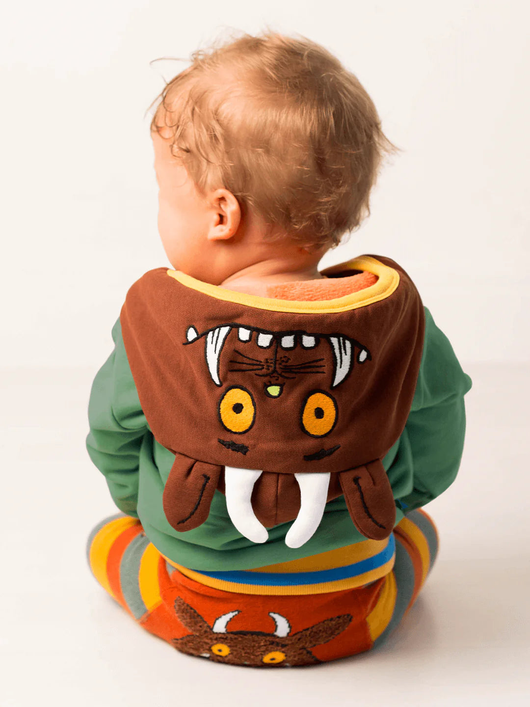 Child wearing a colorful outfit with a gruffalo-themed hoodie and leggings on a white background