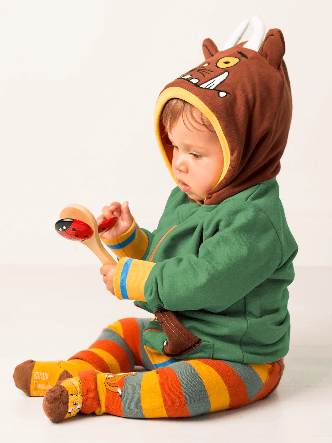 Child wearing a green and brown gruffalo-themed outfit with striped socks, sitting on a white background.