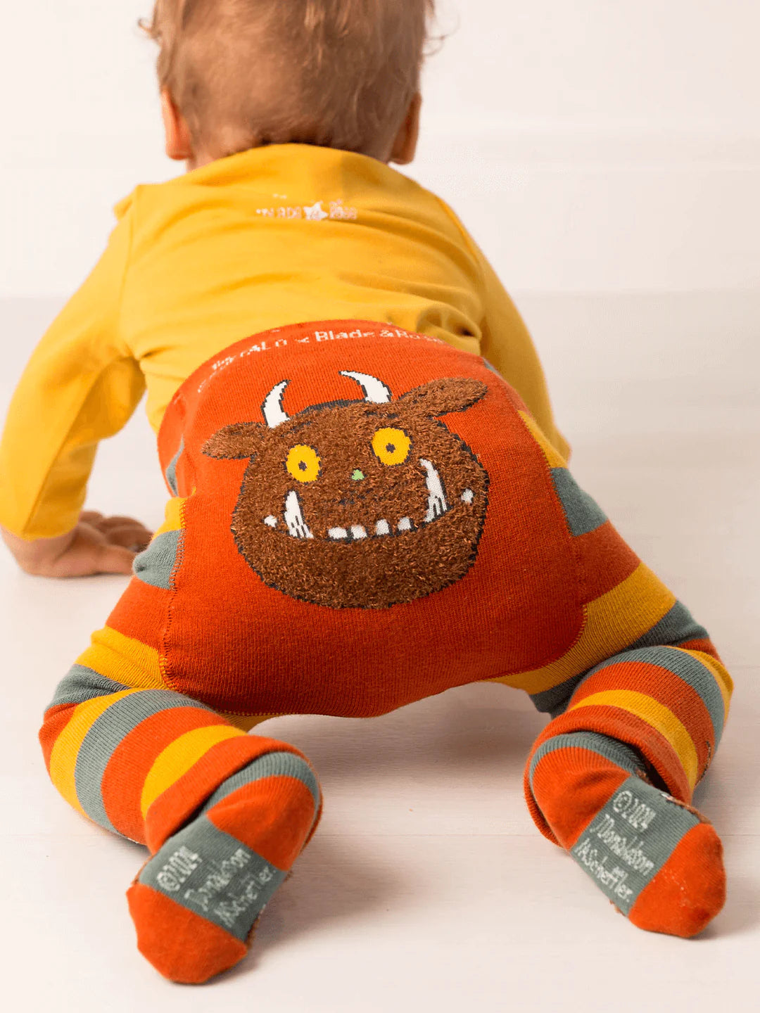 Baby wearing a bright orange outfit with a Gruffalo character on a white background