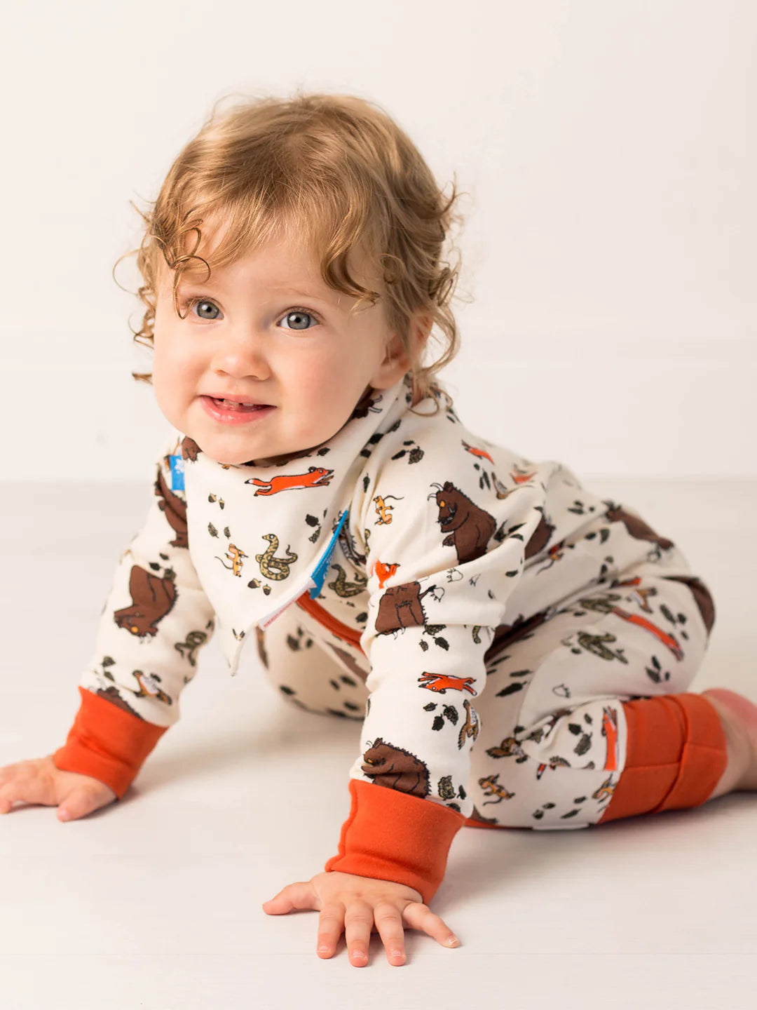 Baby wearing a patterned onesie with orange cuffs on a white background