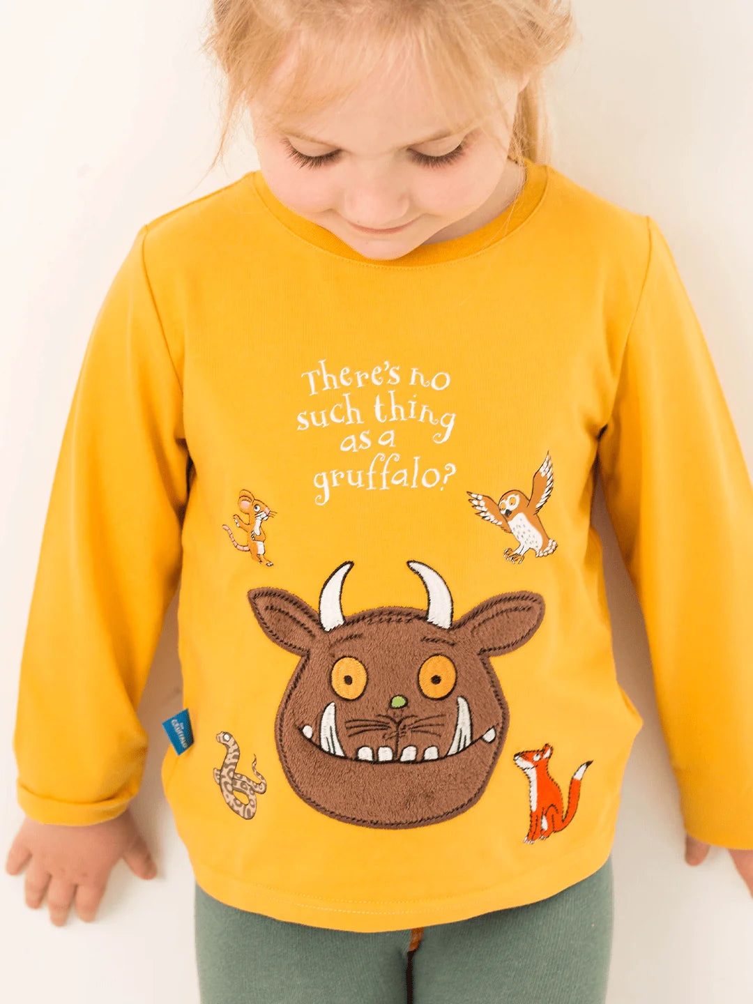Child wearing a yellow shirt with a gruffalo picture and text, standing against a plain background.