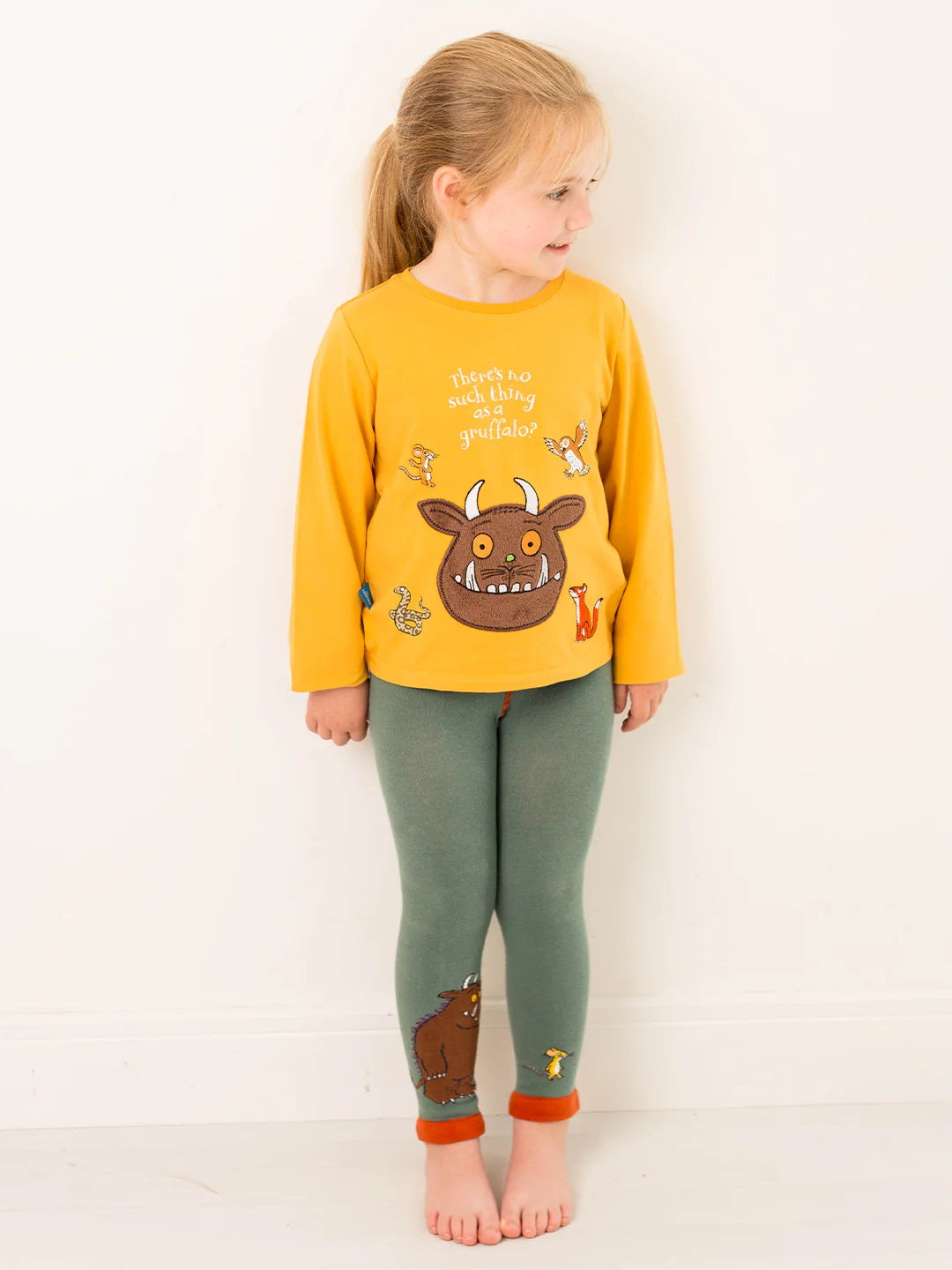 Child wearing a yellow long-sleeve Gruffalo tshirt and green leggings with cartoon designs on a white background