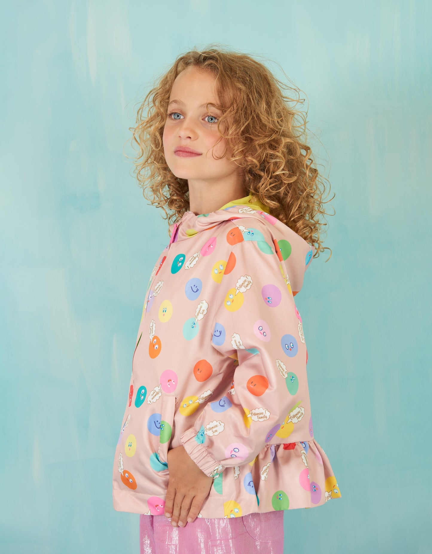 Young girl wearing a pink raincoat with colorful smile patterns against a light blue background