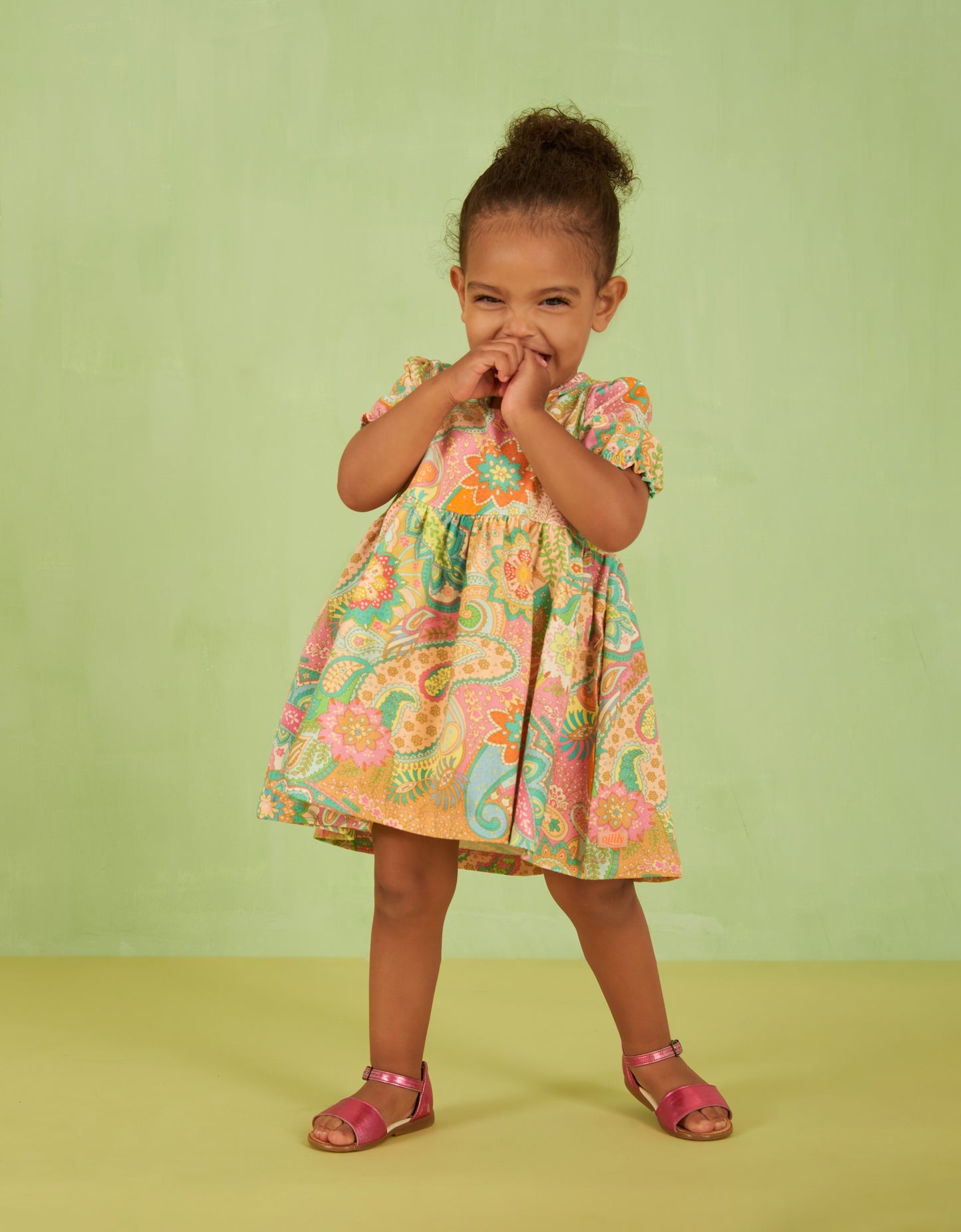 Young girl wearing a colorful floral paisley dress against a green background