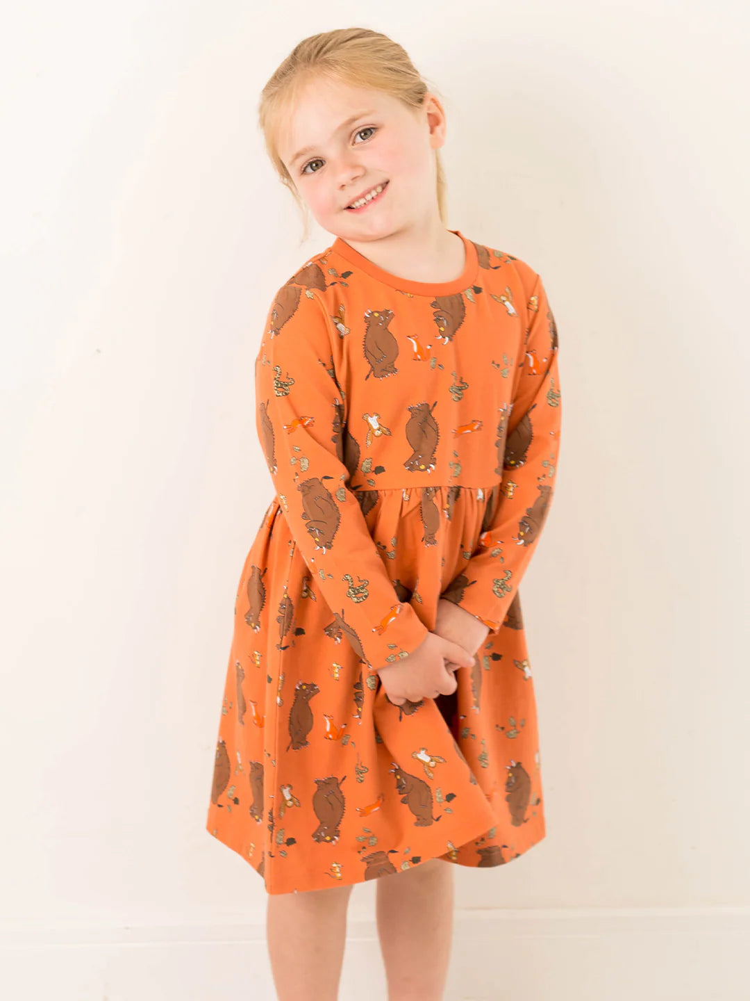 Young girl wearing an orange dress with Gruffalo pattern against a white background