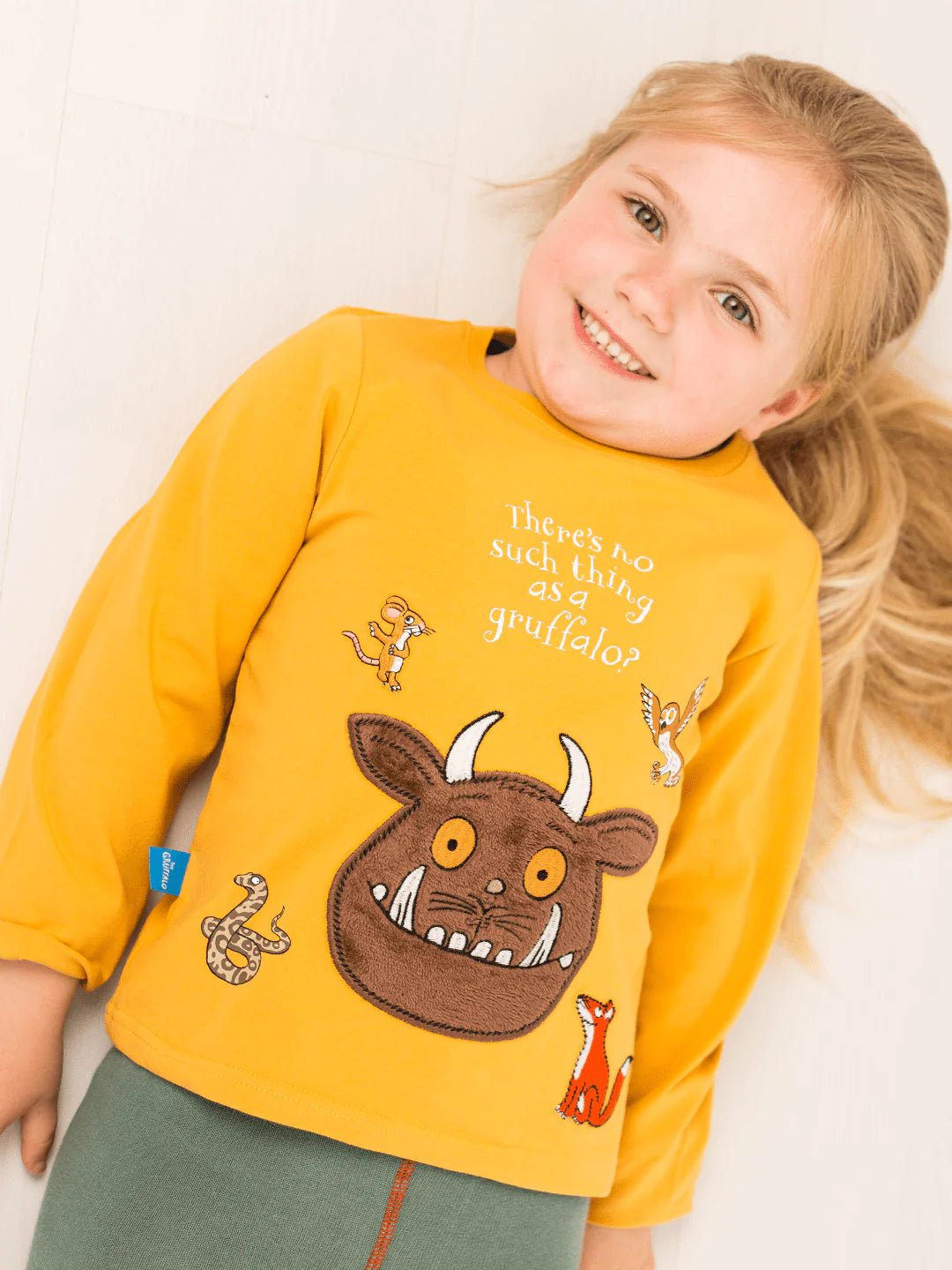 Child wearing a yellow tshirt with a gruffalo character design on a plain background