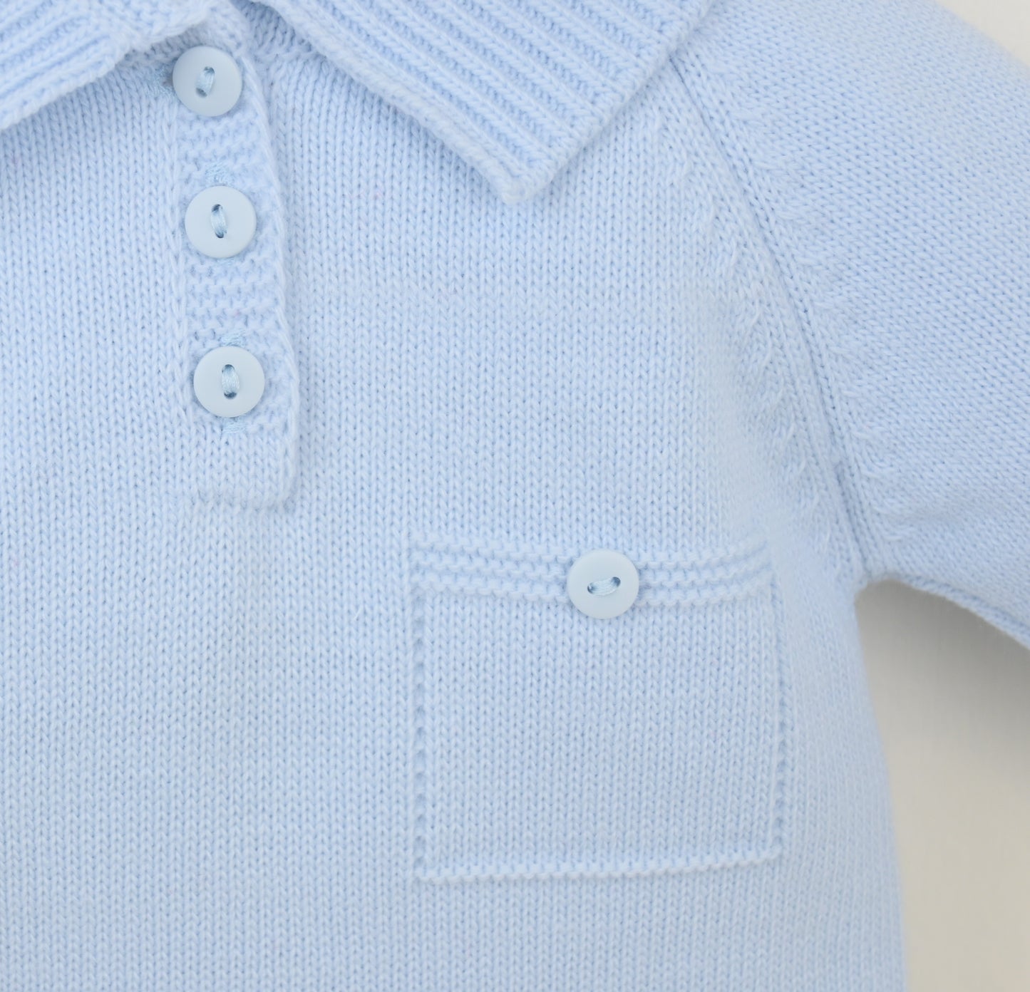 Light blue knitted baby outfit with buttons on a beige background