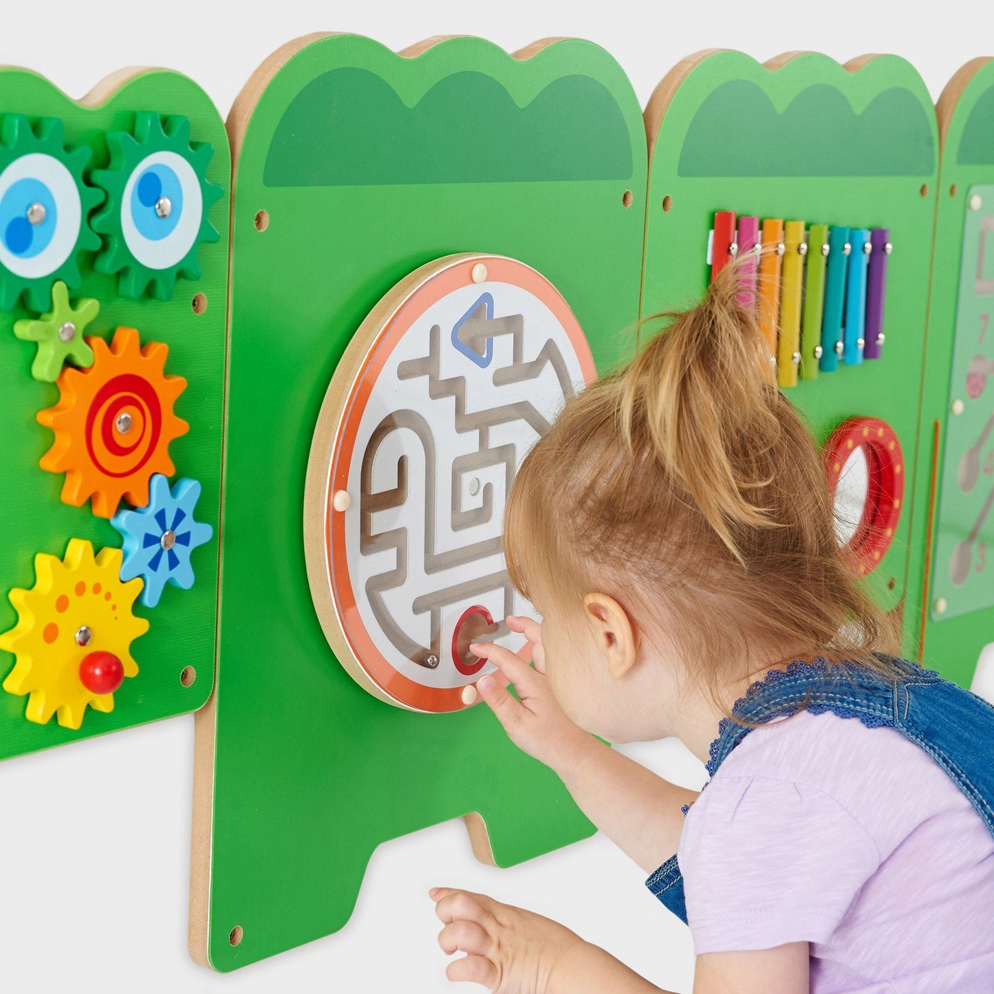 Child playing with a colorful educational wall panel featuring gears and a maze.