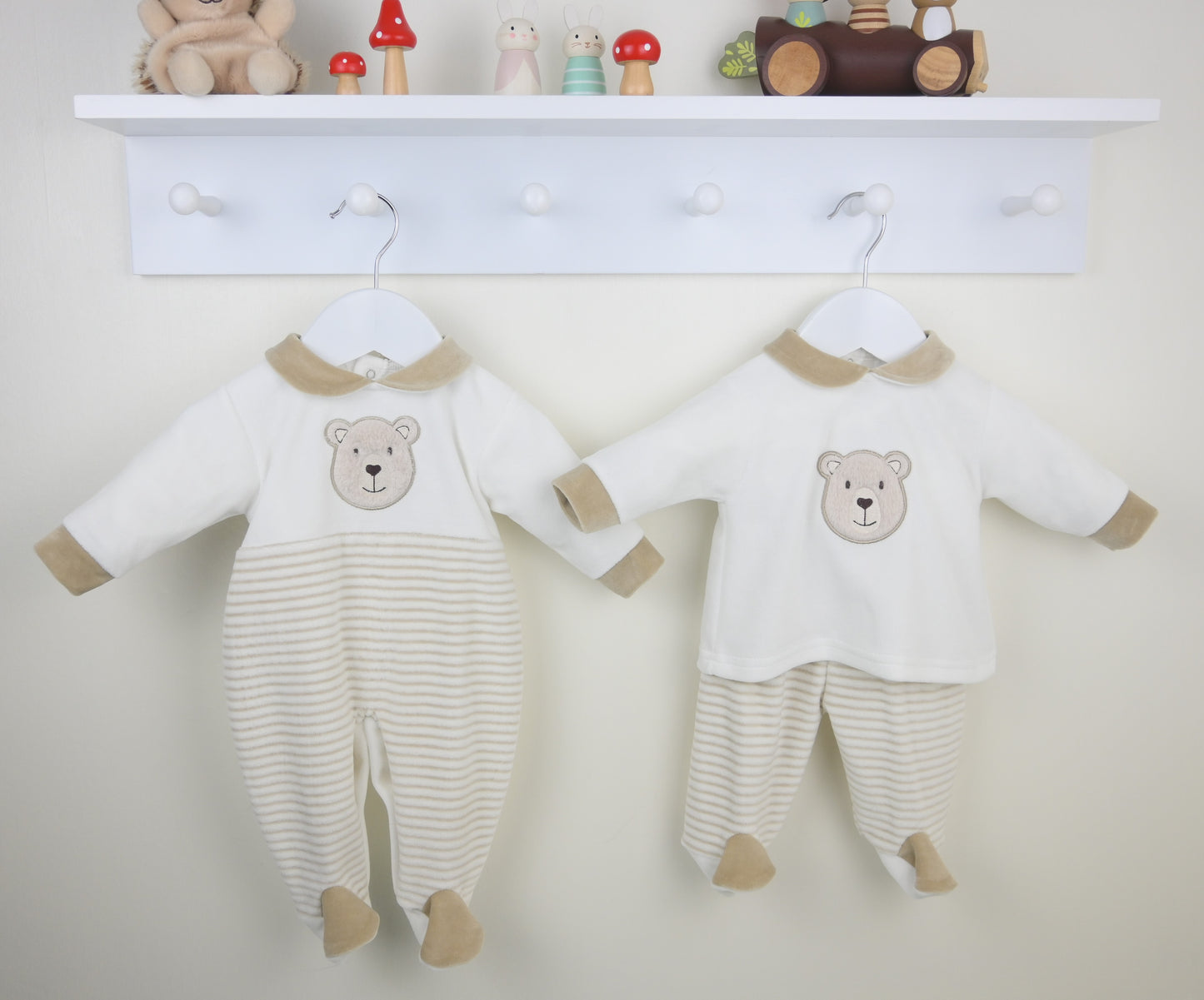 Two baby rompers with bear designs hanging on a white wall.