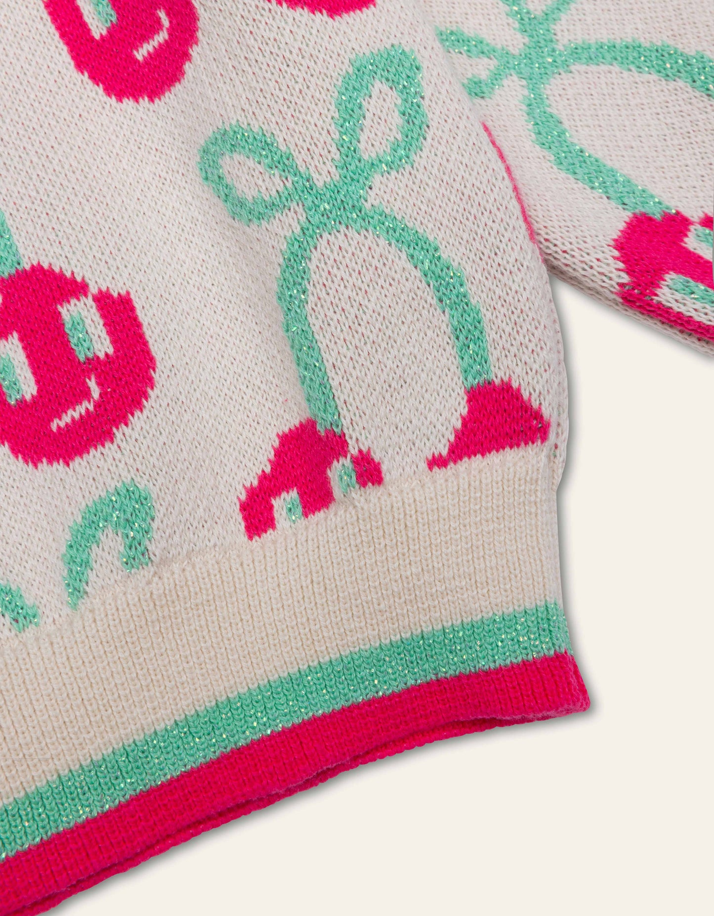 Close-up of a knitted garment with pink and green cherry patterns on a light background