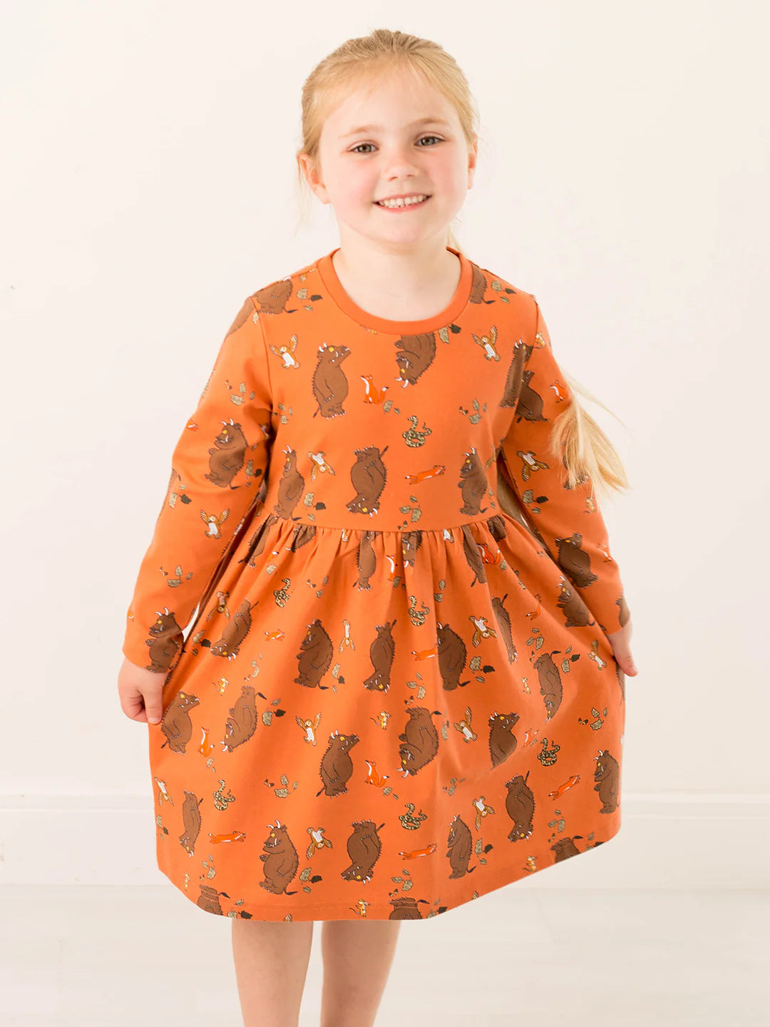 Young girl wearing an orange dress with brown gruffalo patterns on a white background
