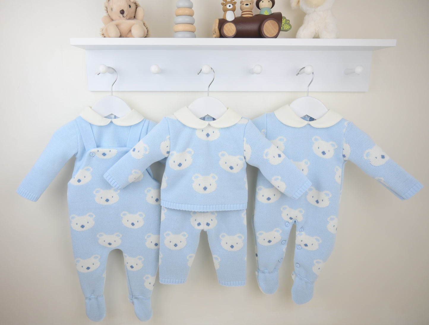 Set of blue baby rompers with bear patterns hanging on a white coat rack.