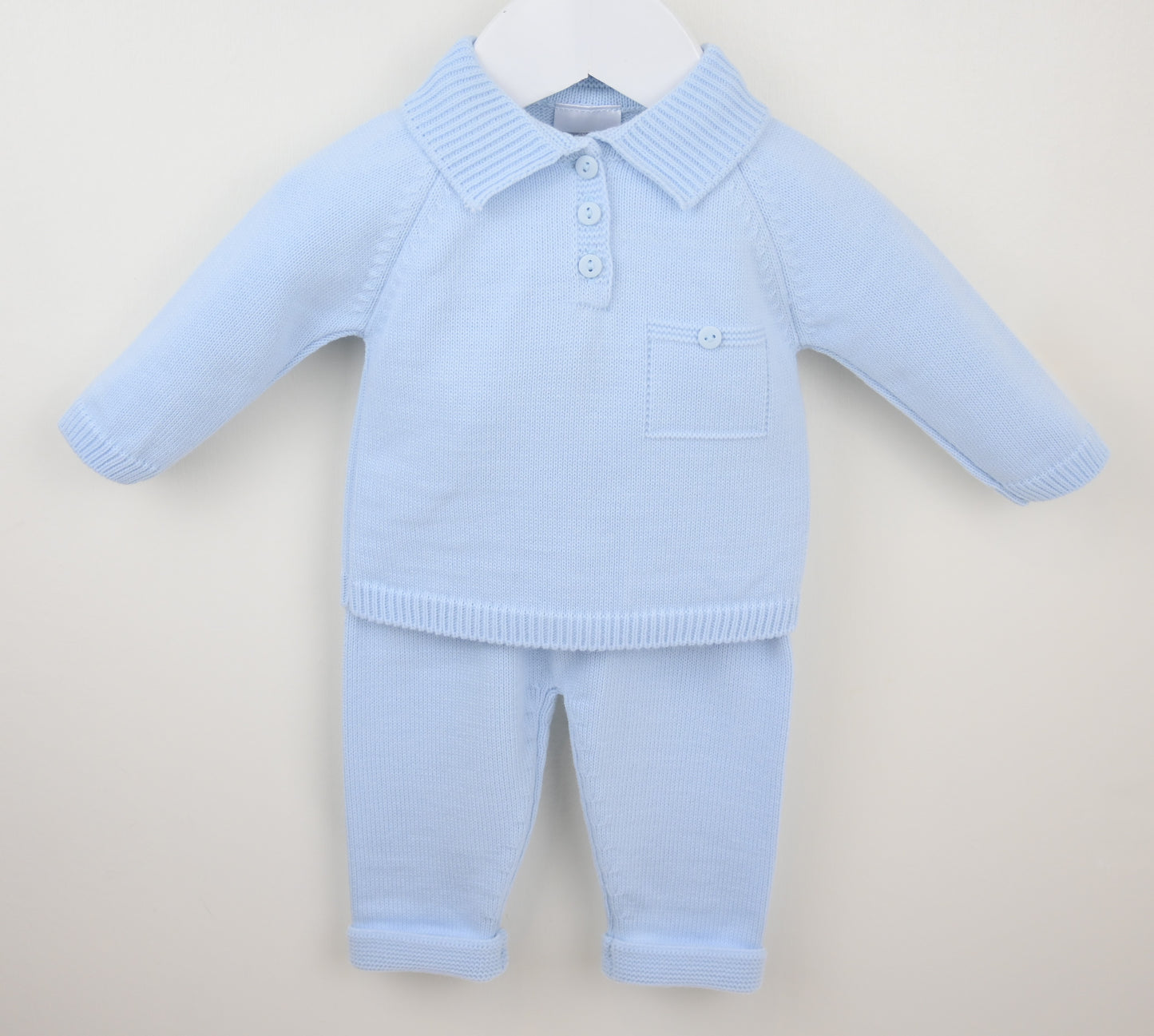 Light blue knitted baby outfit with a shirt and pants on a beige background