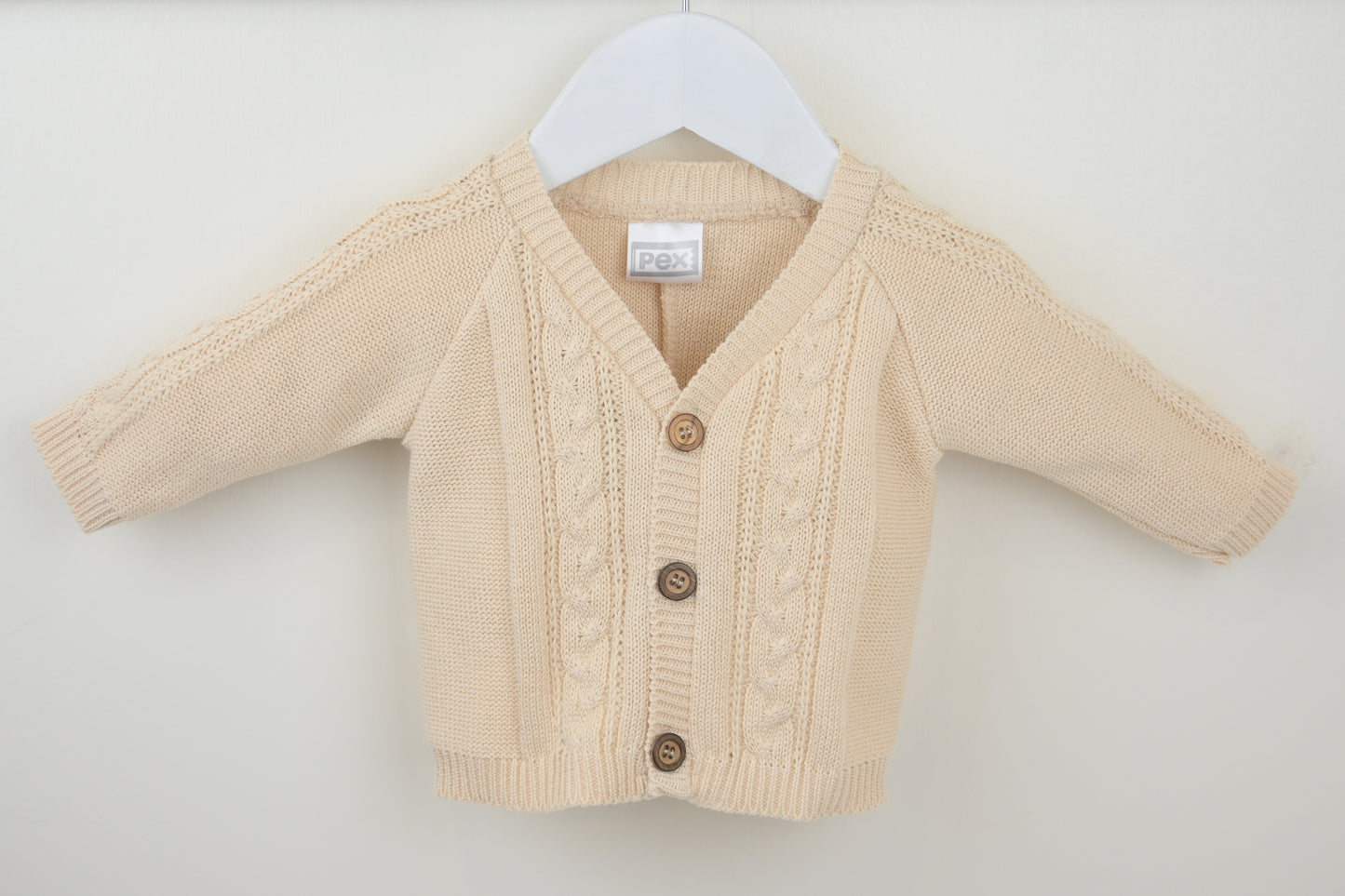 Beige baby cardigan on a white hanger against a white background