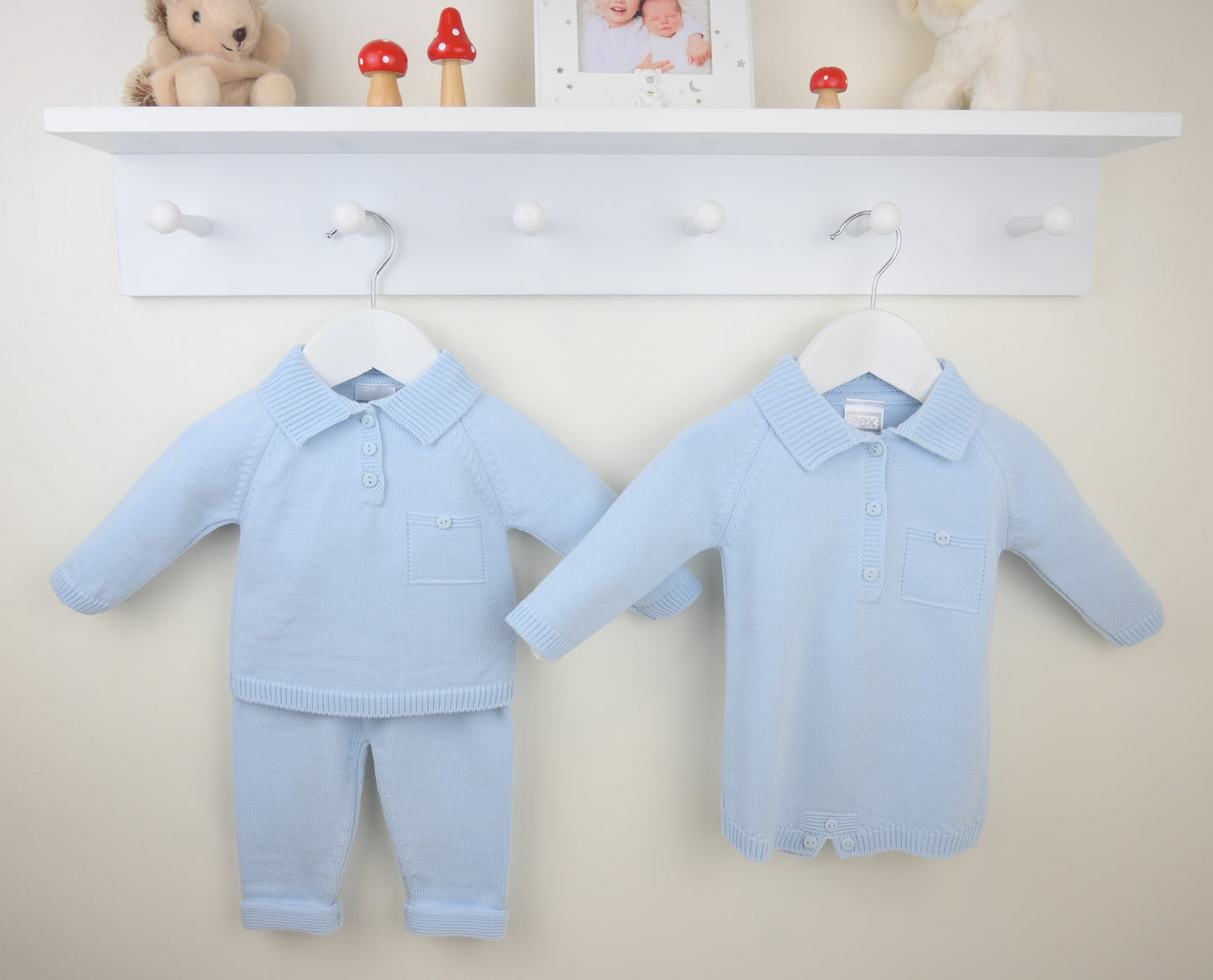 Light blue baby outfits on hangers against a white wall with a shelf in the background.