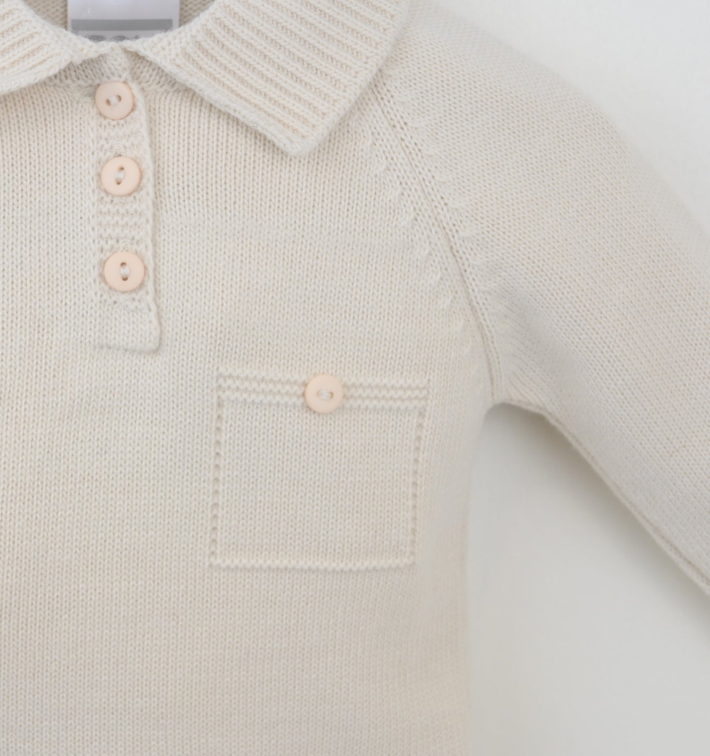 Close-up of a light-colored knitted baby outfit with buttons on a white background
