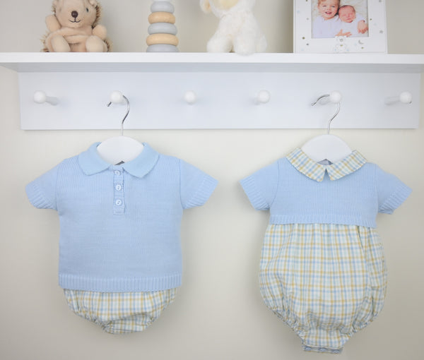 Two baby rompers hanging on a white wall with toys and a photo frame in the background.