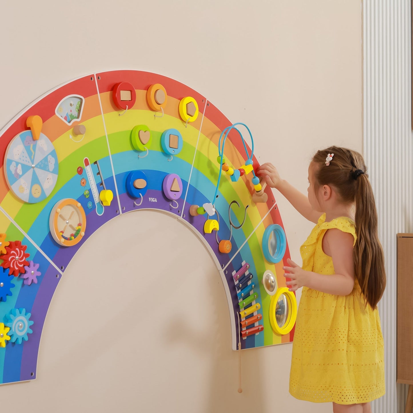 Child playing with a colorful rainbow-shaped educational toy on a wall.