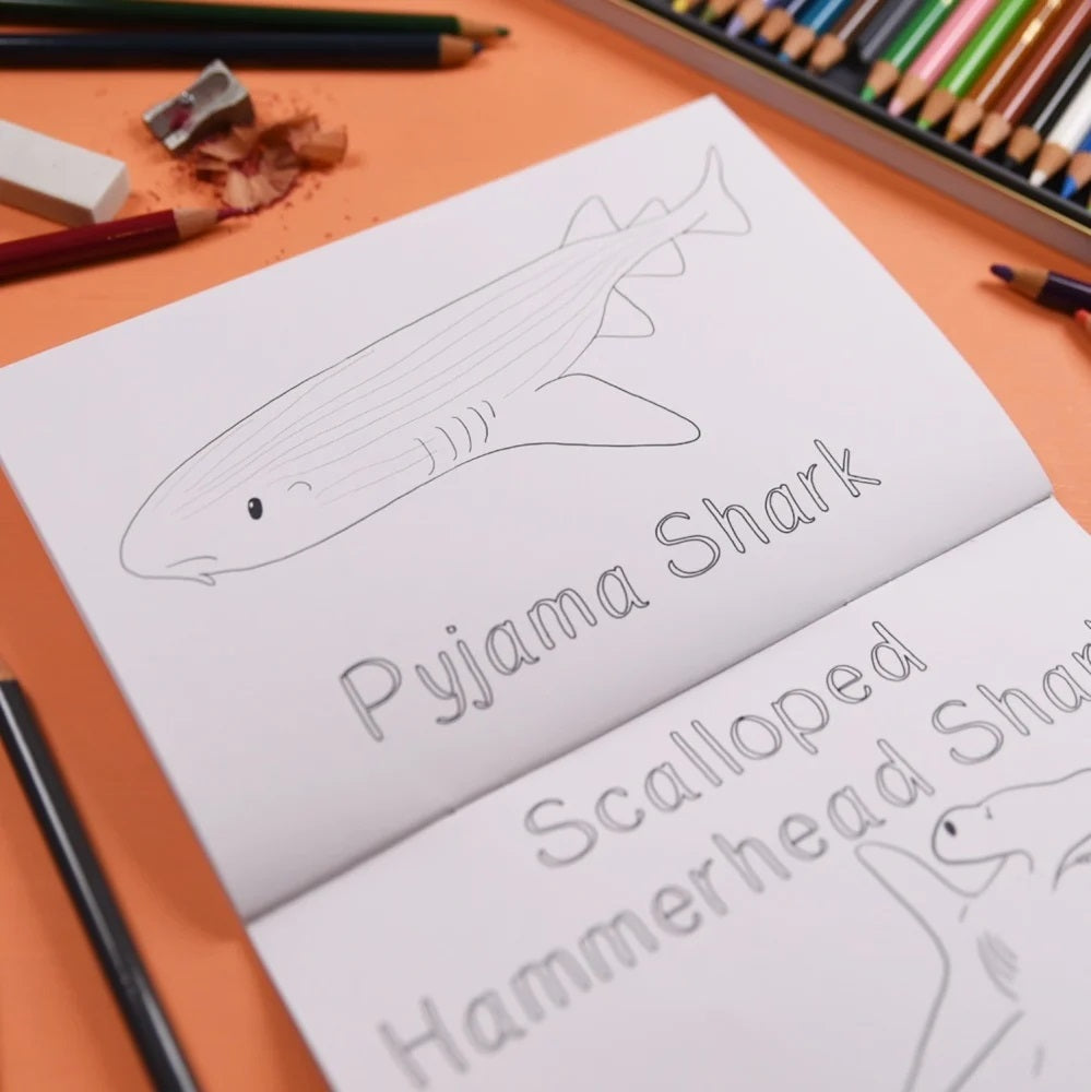 Children's coloring book with shark illustrations and coloring tools on a table.