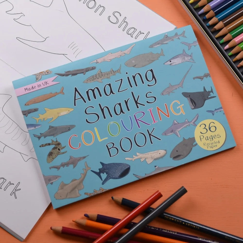 Coloring book titled 'Amazing Sharks' with colored pencils on an orange surface