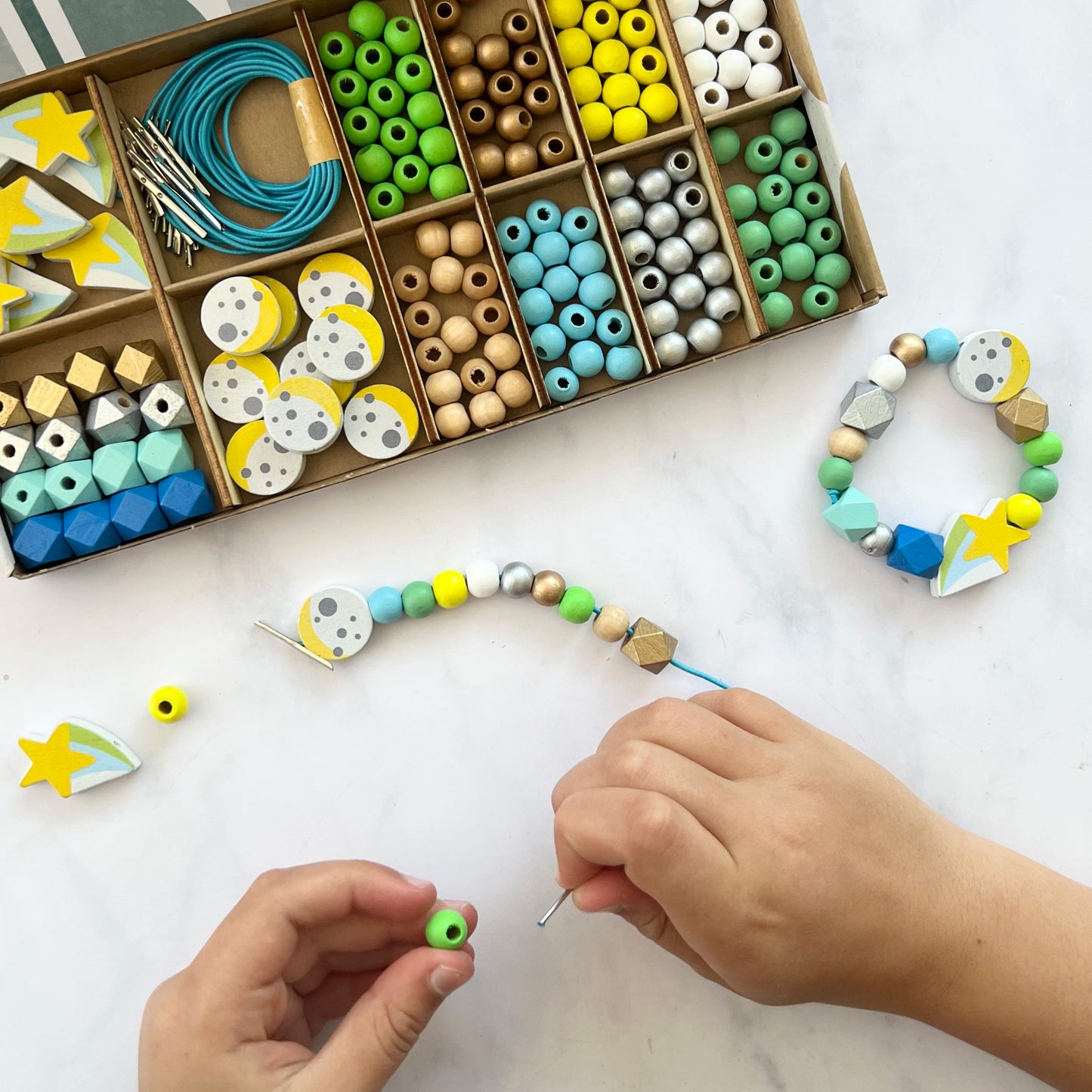 Beads and jewelry-making tools on a table with a child's hands working on a bracelet.