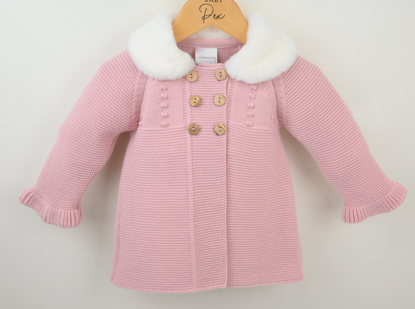 Pink knitted coat with white fur collar on a hanger against a light background