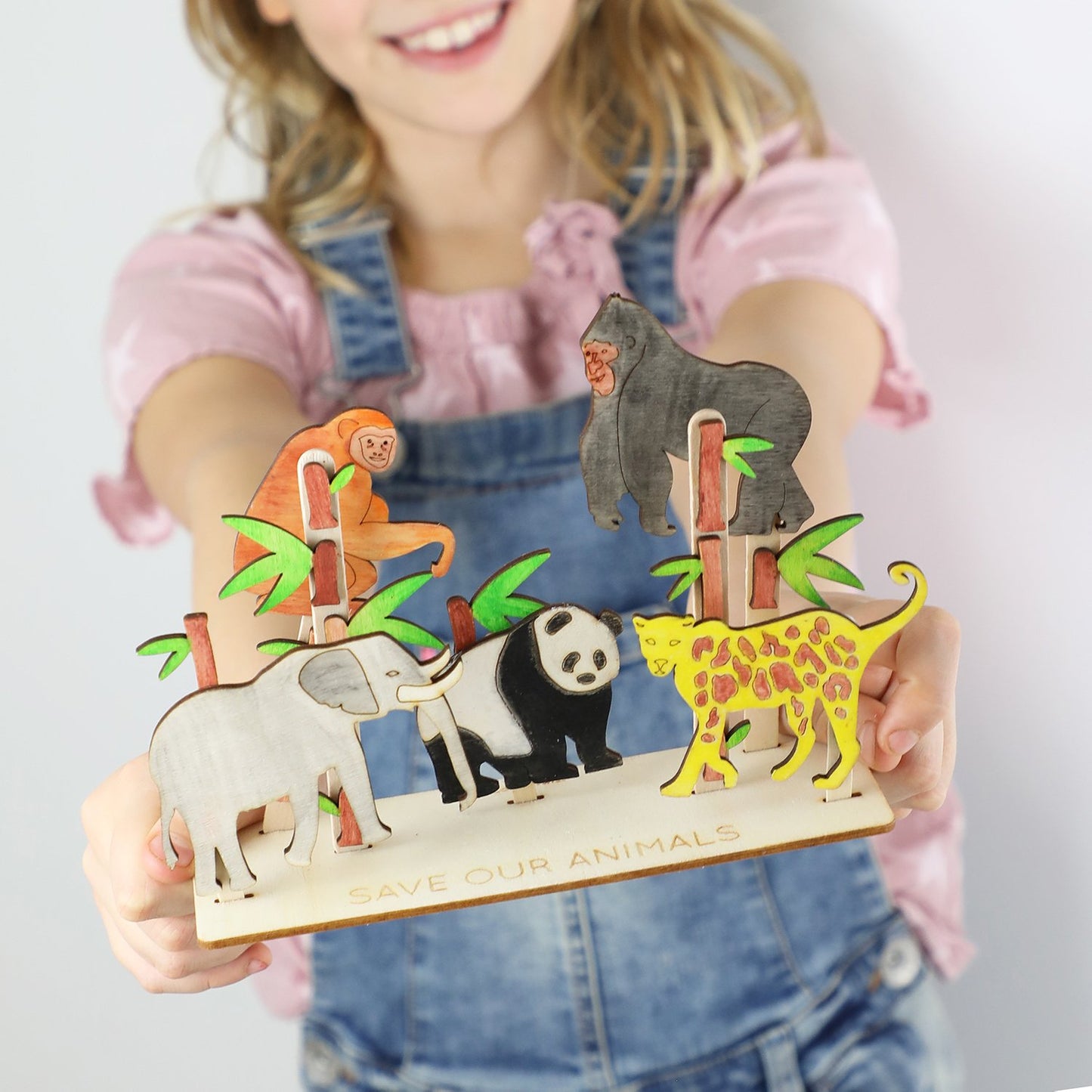 Child holding a wooden toy with animal figures and 'Save Our Animals' text
