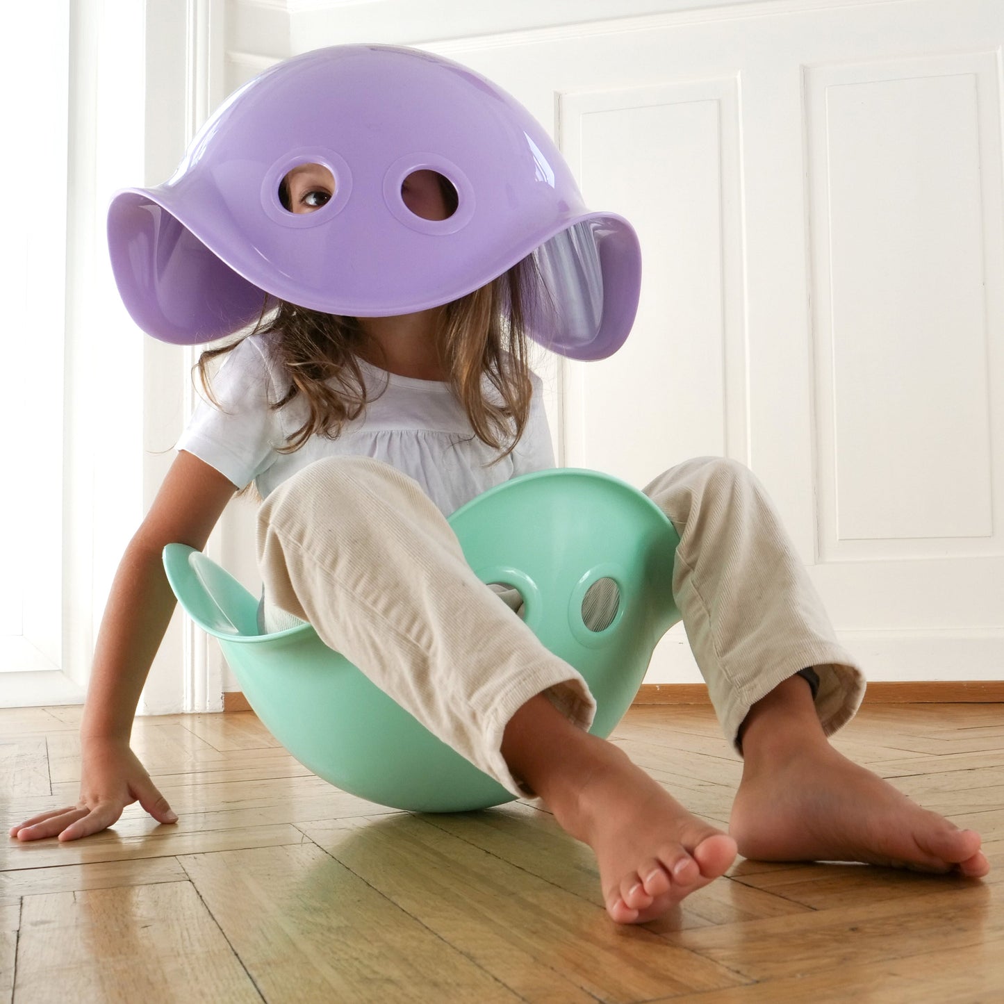 Child sitting on a green bilibo with a purple bilibo on head.
