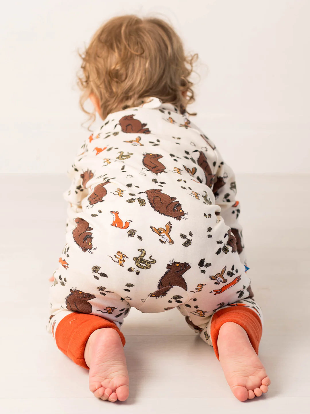 Child wearing a patterned onesie with gruffalo designs on a plain background