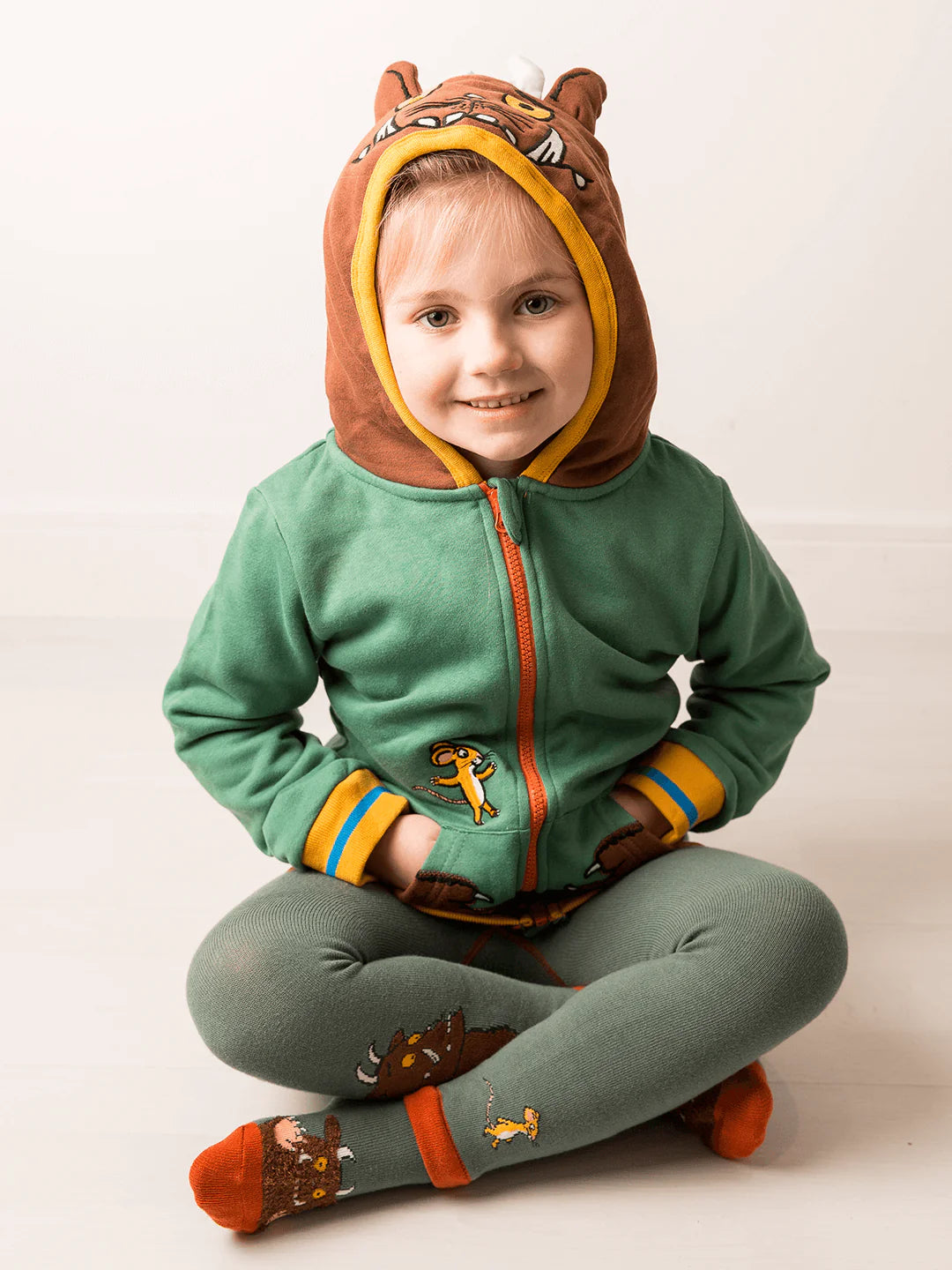 Child wearing a green and brown gruffalo-themed outfit with a hood on a white background